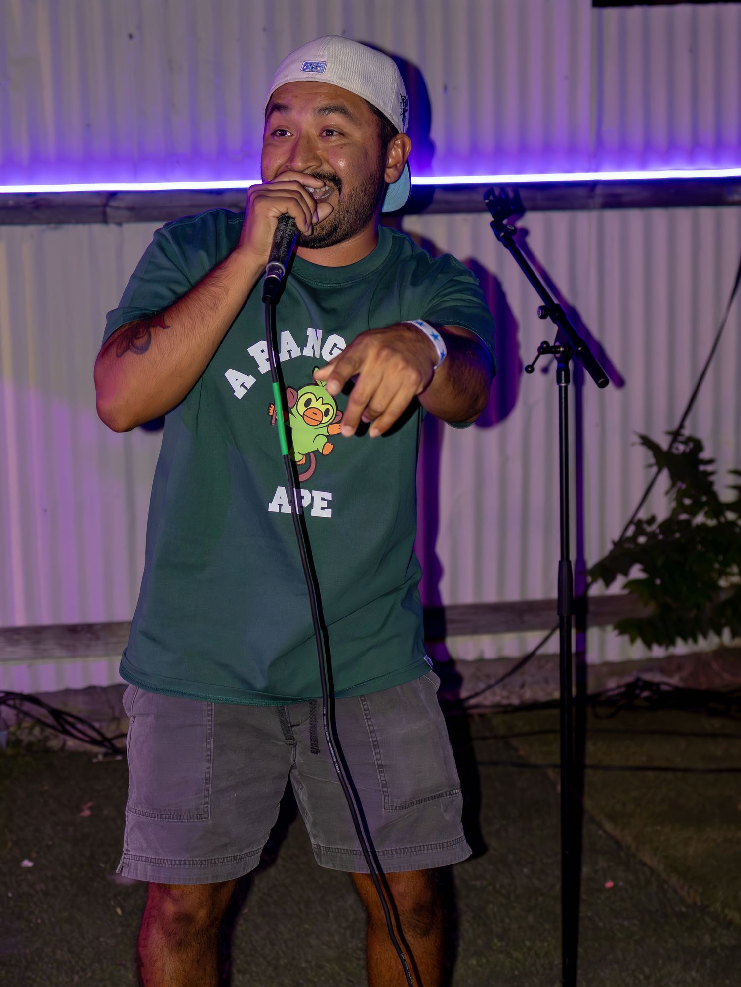 Performer in green BAPE shirt and shorts gestures while performing with microphone on stage.