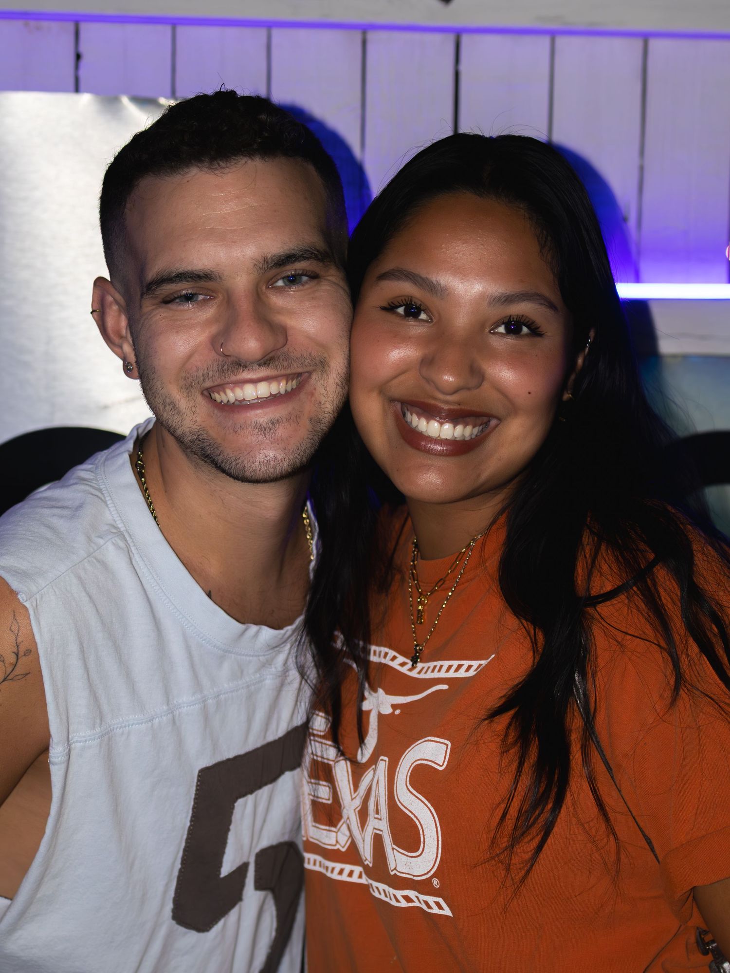 Couple in casual attire smiling together at nighttime event with blue lighting.
