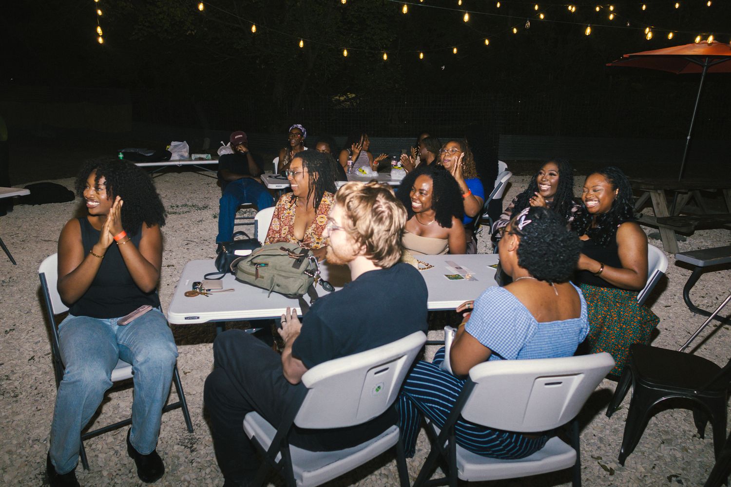 People seated at communal tables during a casual outdoor nighttime gathering.