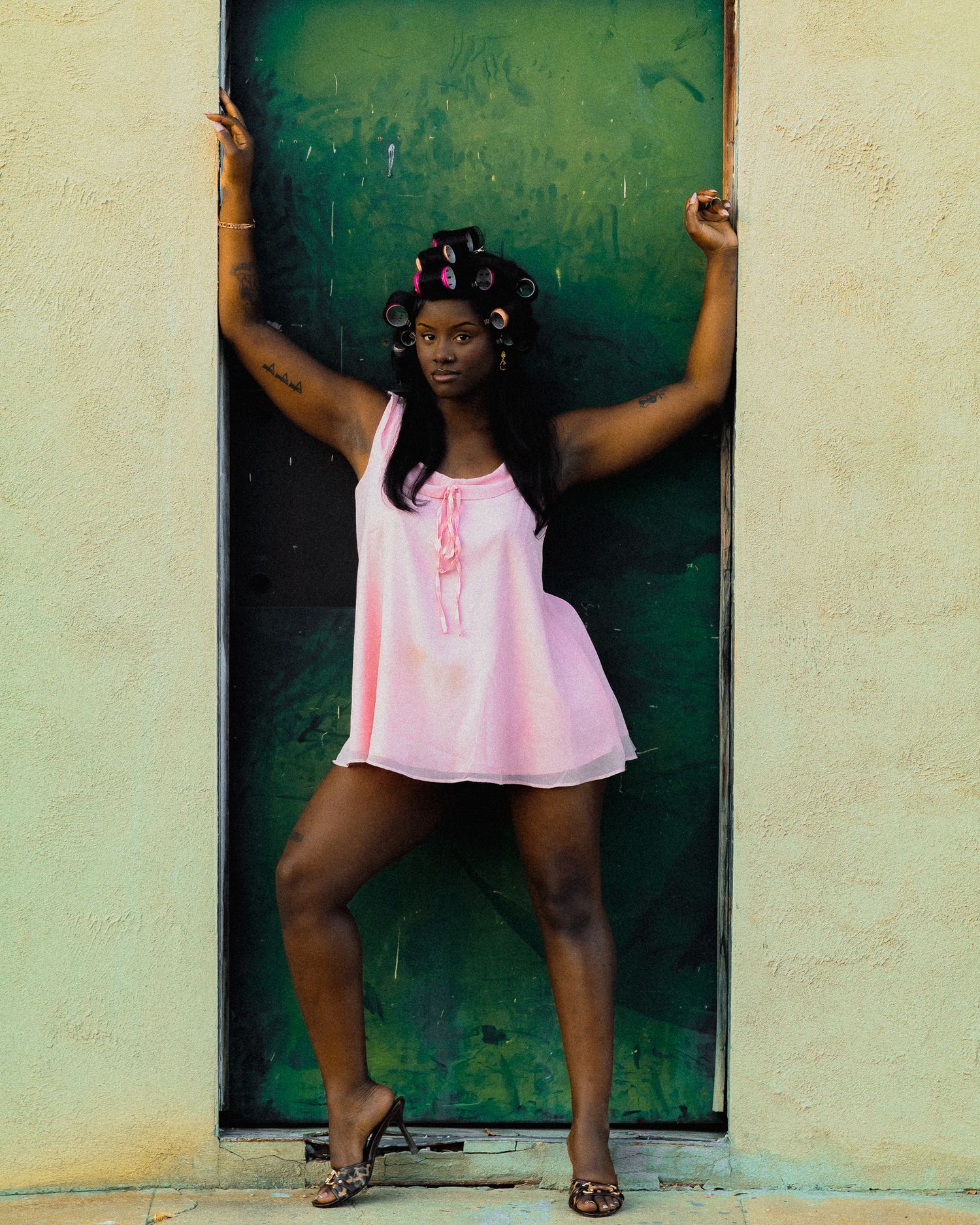 Model strikes dynamic pose in pink dress against green doorway.