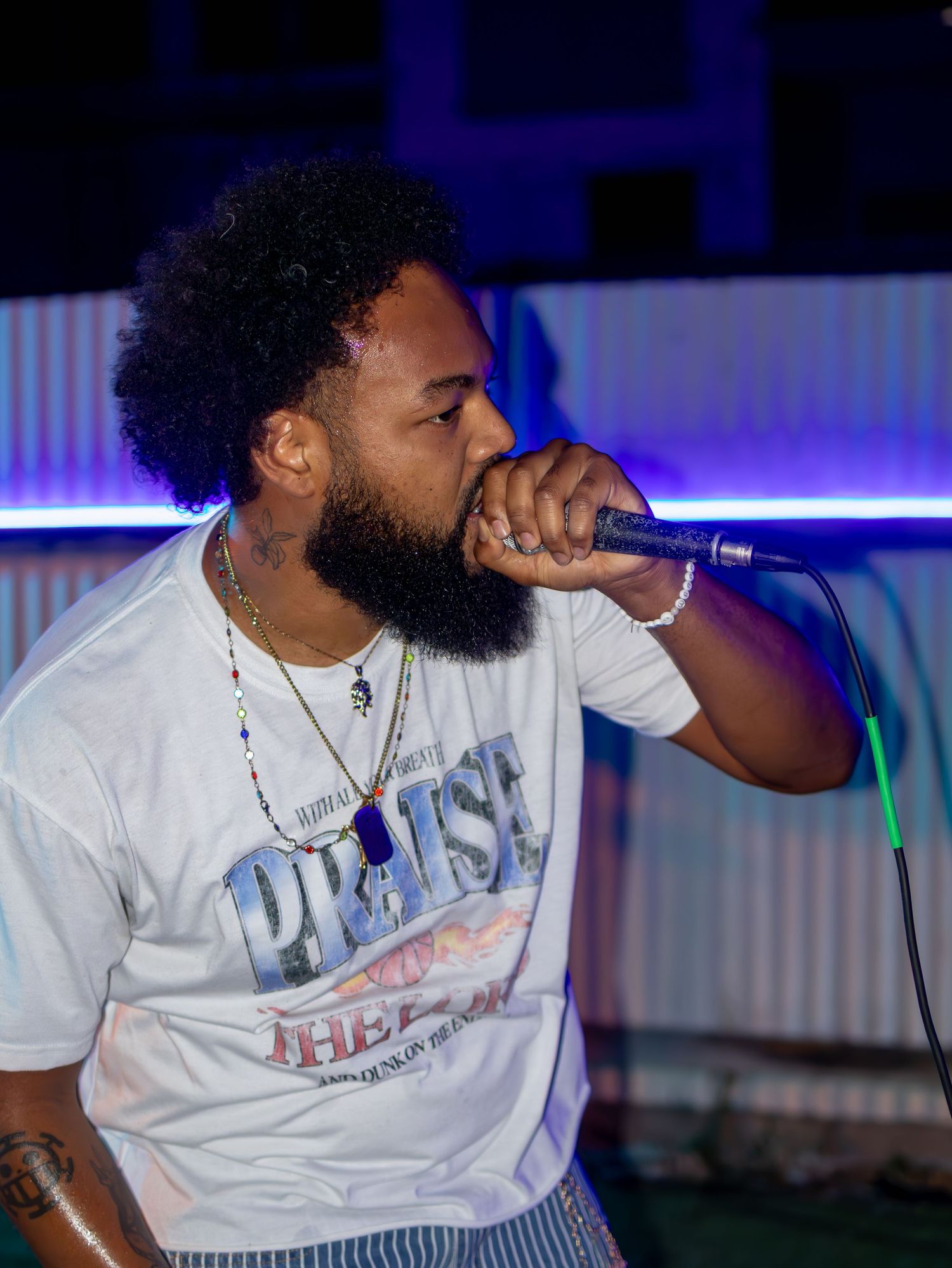 Performer in striped pants and white tee energetically singing under purple stage lights.