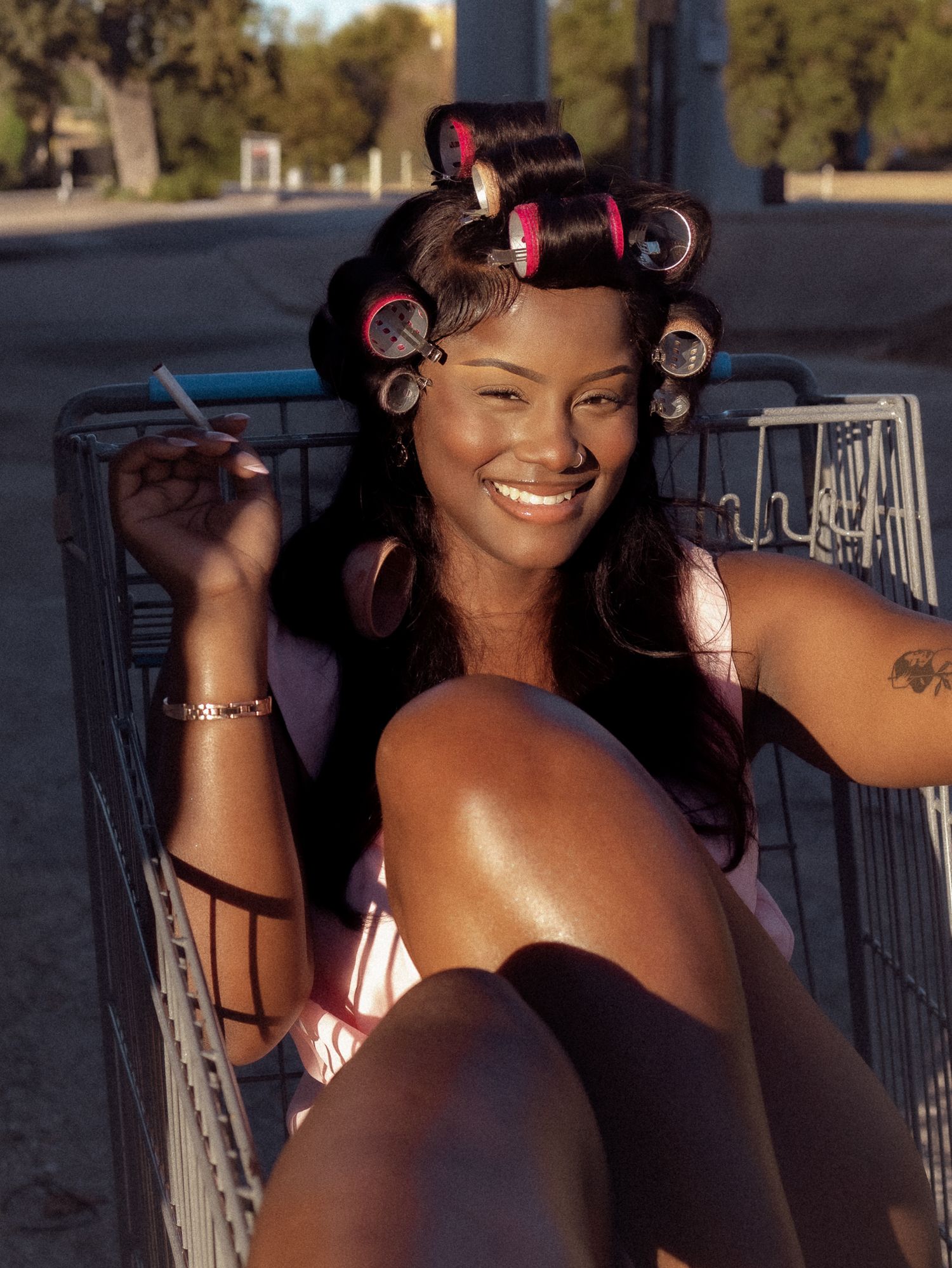 Woman in pink rollers poses against rustic outdoor railing.