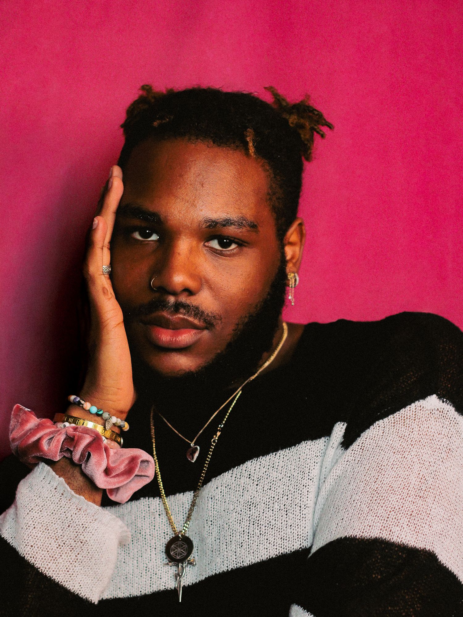Fashion portrait featuring gray sweater and gold jewelry against pink backdrop.