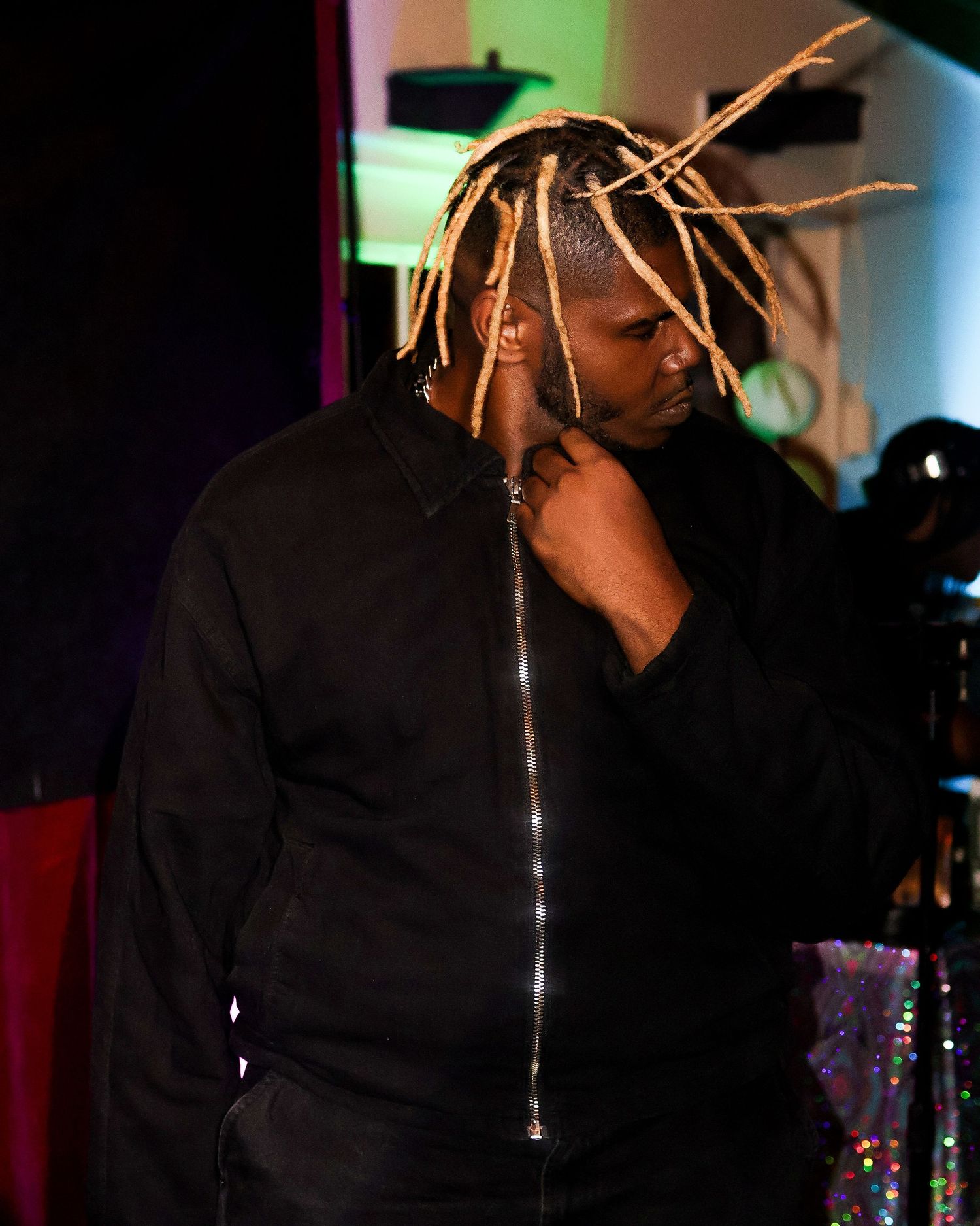 Artist in black jacket performing on stage with dramatic lighting and background effects.