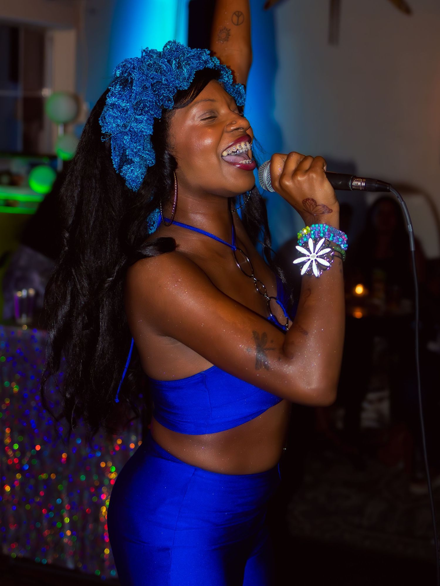 A performer in royal blue delivers an animated performance under colorful stage lights.