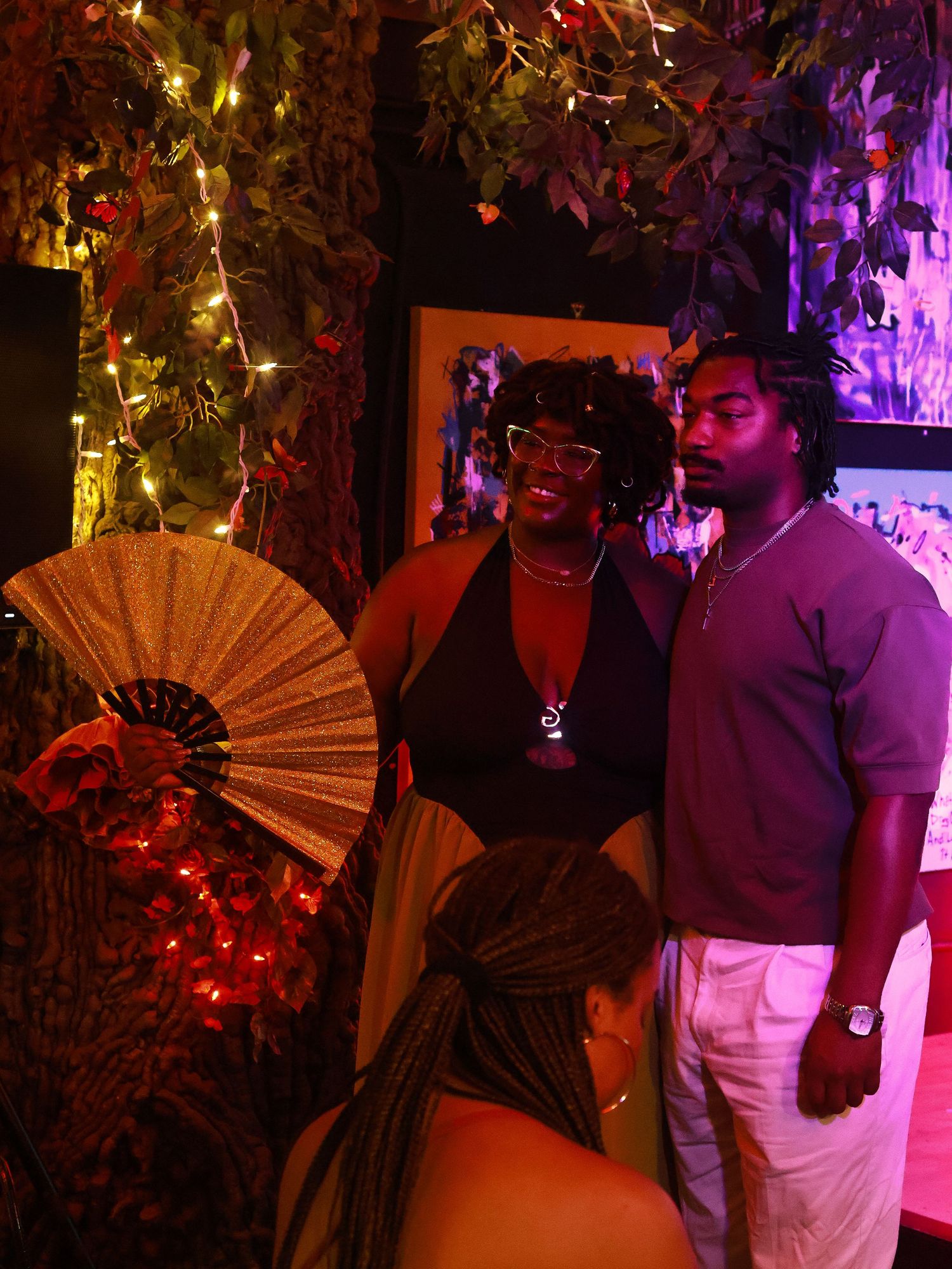 Partygoers with a decorative fan in a dimly lit venue with colorful ambient lighting.