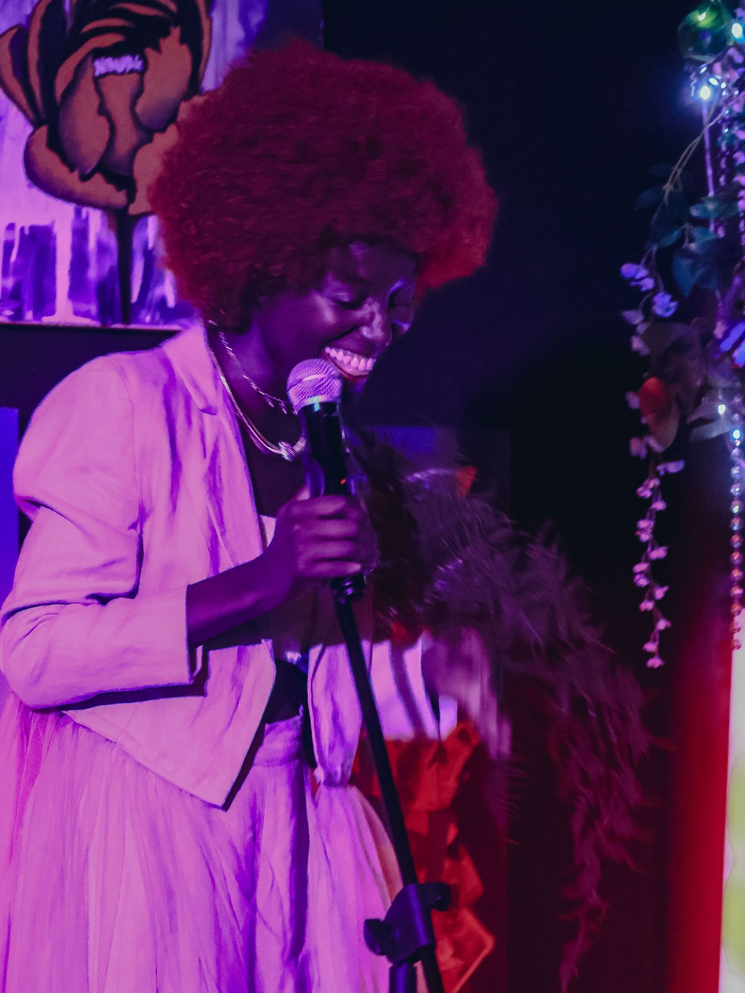 A performer in white attire sings into a microphone under dramatic purple stage lighting.