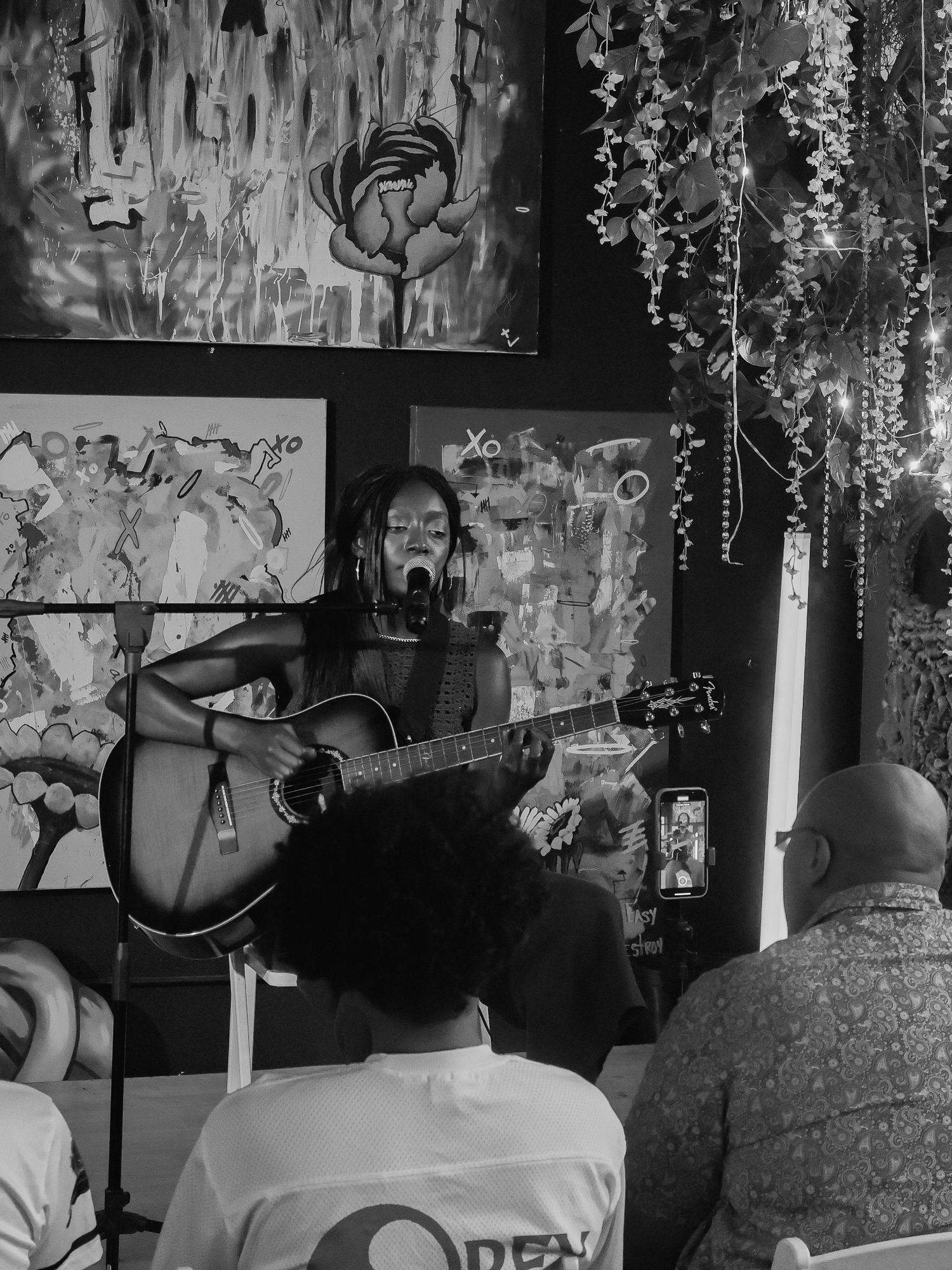 Grayscale image captures audience members seated during intimate musical performance.
