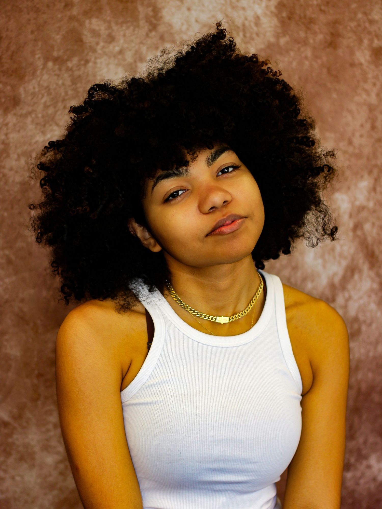 Natural curly hair styled with white tank top against brown studio background.