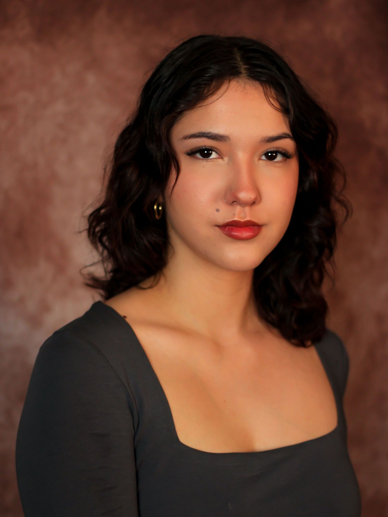 Elegant portrait in black dress with red lipstick against brown background.
