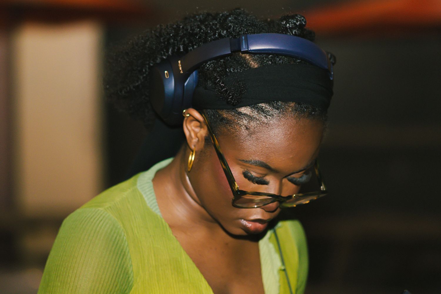 DJ working behind equipment in a yellow gradient shirt and glasses at a nighttime event.
