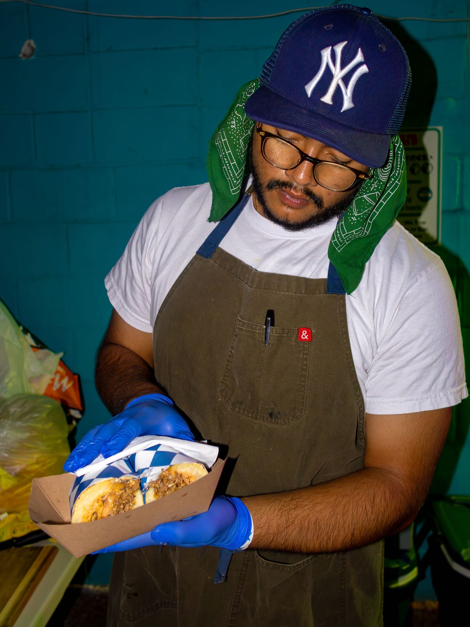 Restaurant worker in Yankees cap and apron preparing food in kitchen with blue gloves.