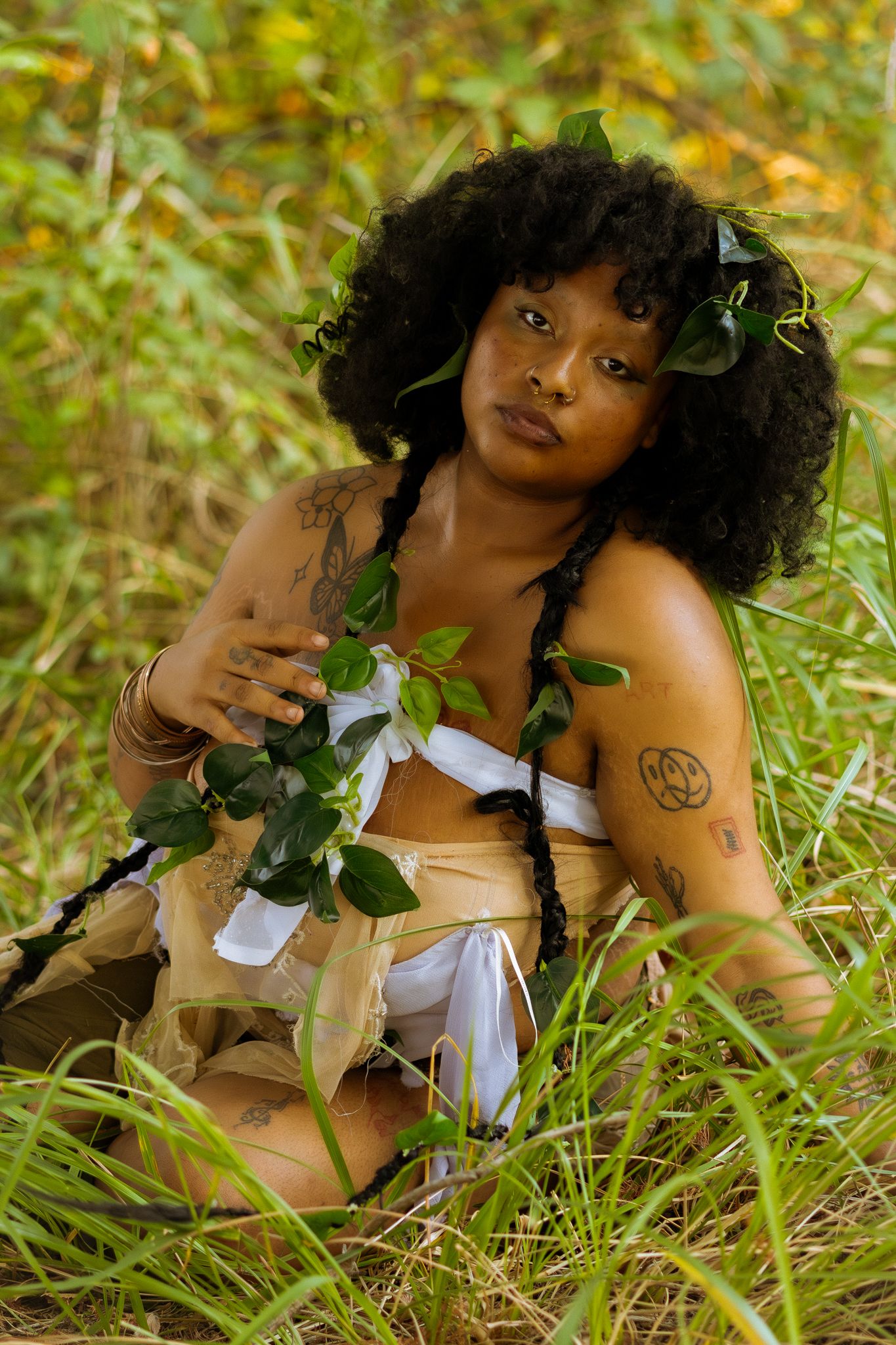 Artistic portrait surrounded by green foliage wearing a white and beige ensemble.