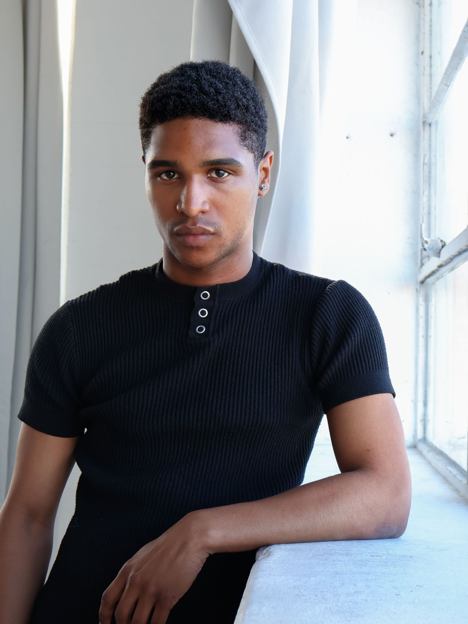 Portrait series in black ribbed shirt against white interior setting.