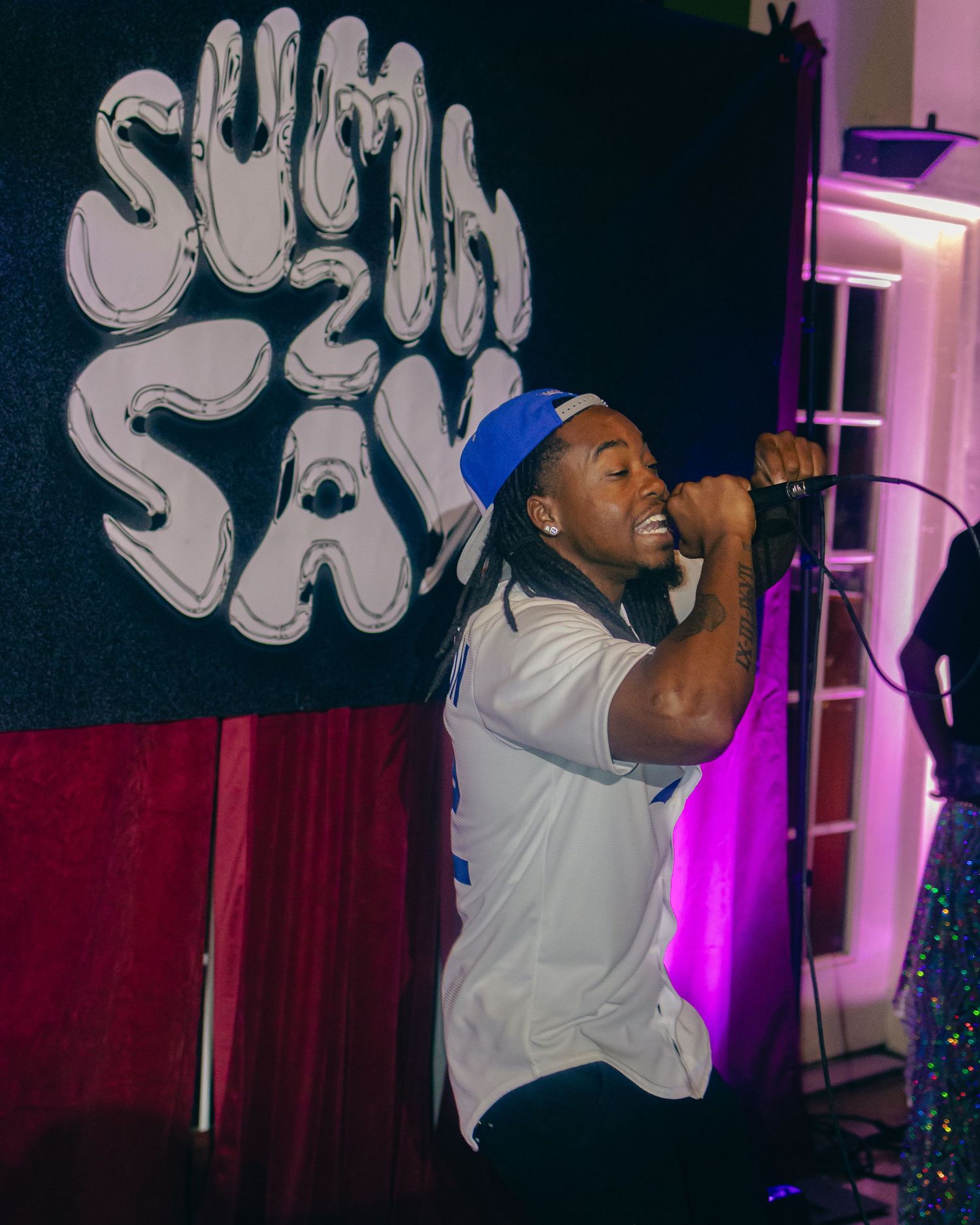 Hip hop artist performs energetically in white jersey under vibrant stage lighting.