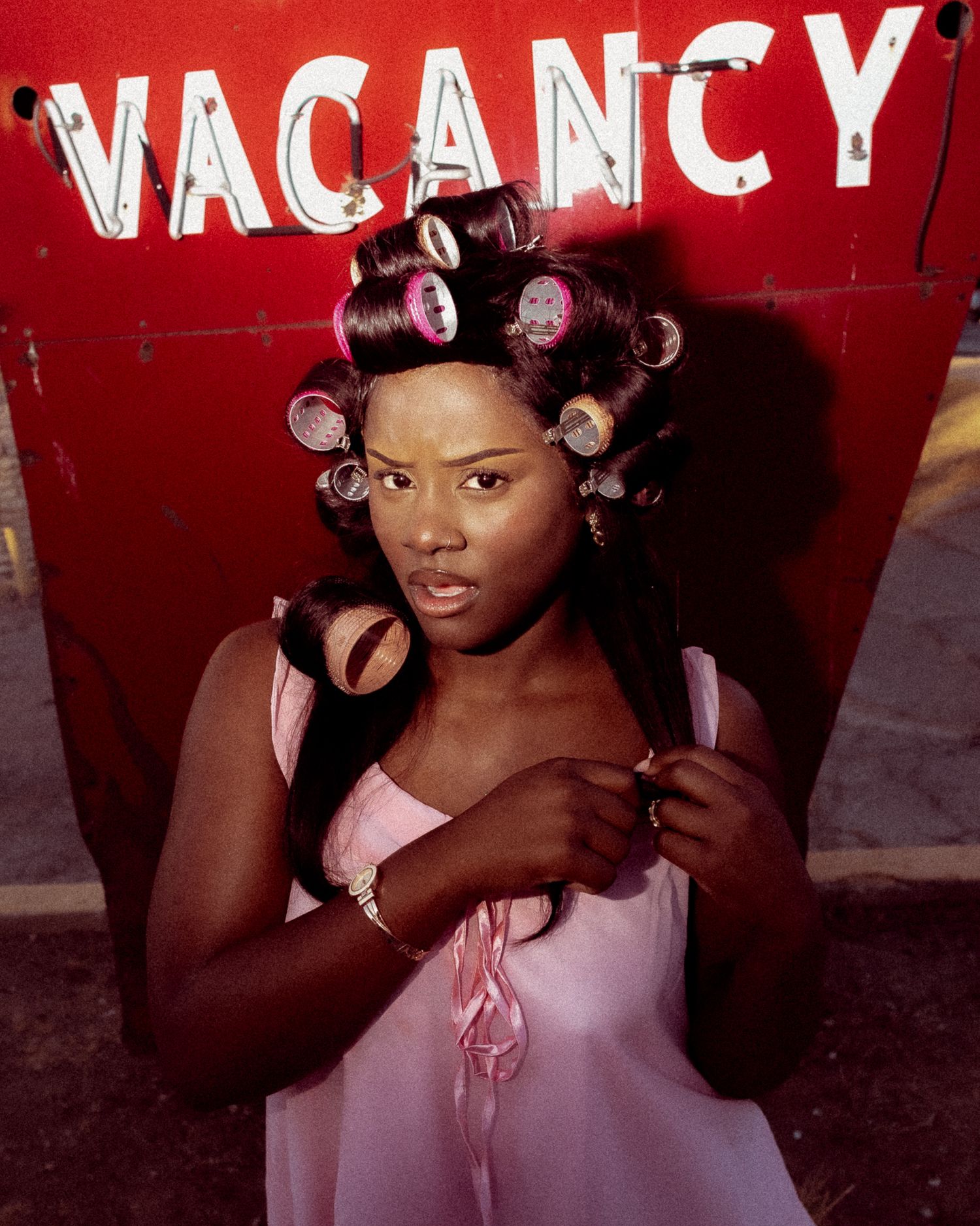 Retro-styled beauty shoot with hair rollers against a bright red vacancy sign.