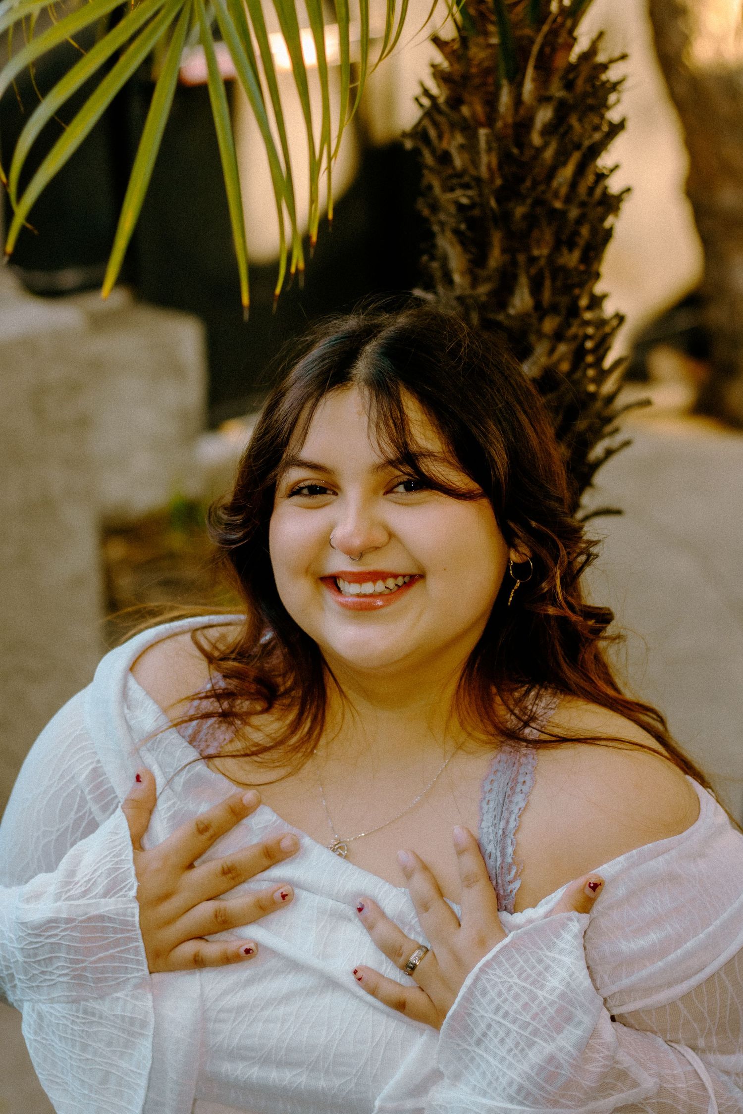 Natural outdoor portrait in white lace dress with palm fronds creating tropical ambiance.