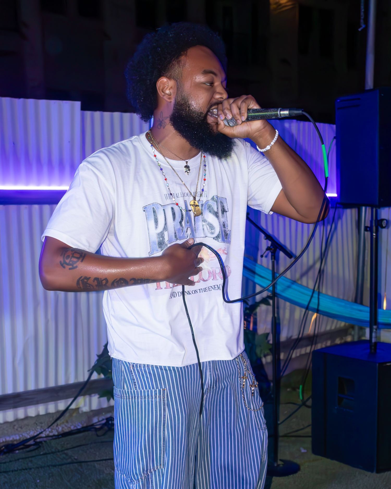 Performer in striped pants and white t-shirt singing on stage with blue lighting.