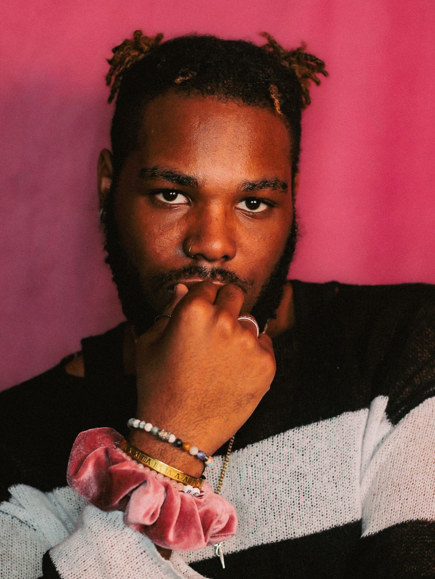 Creative portrait series with pink accent and gray sweater against red wall.