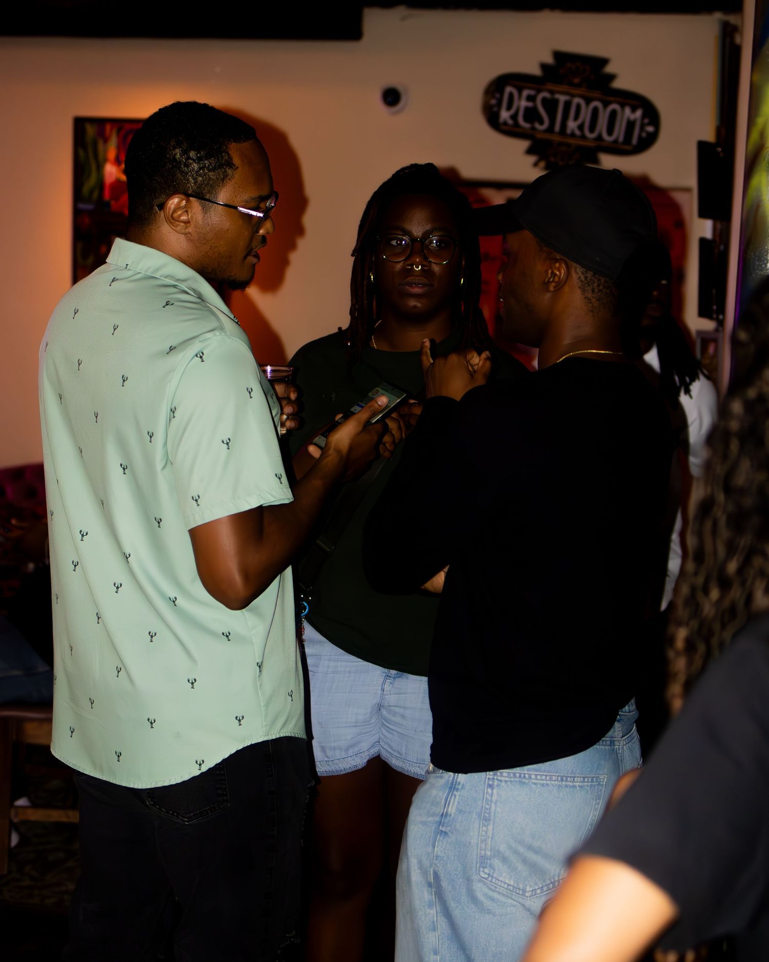 Group of people interacting near a restroom sign in an indoor venue.