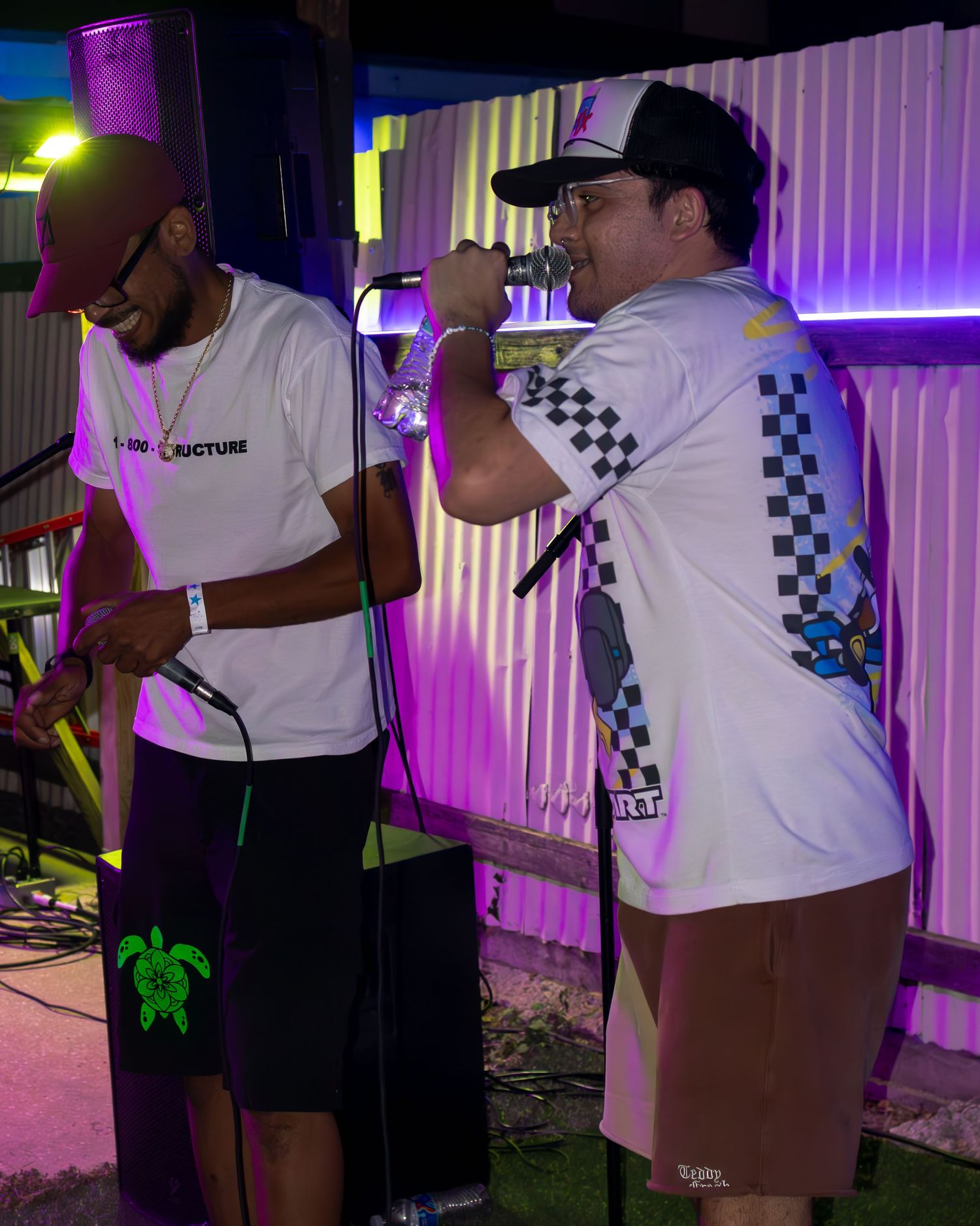 Live performers singing on stage with vibrant neon lighting in the background.
