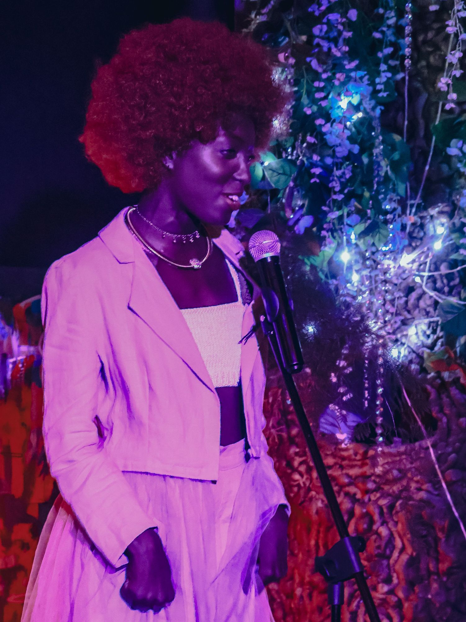 A performer in a white dress sings on stage with purple and blue lighting effects.