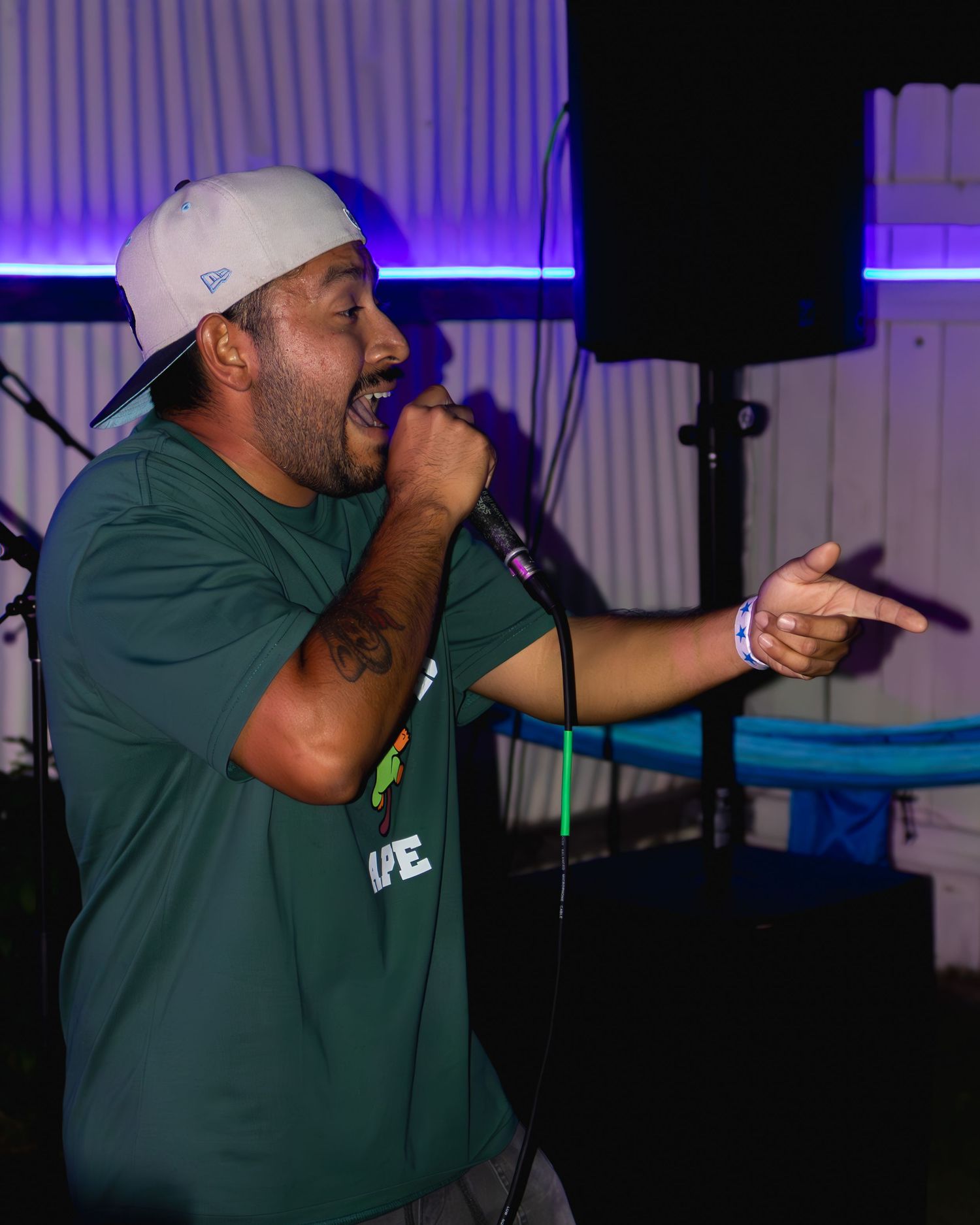 Energetic performer in green shirt gestures while singing into microphone under purple stage lighting.