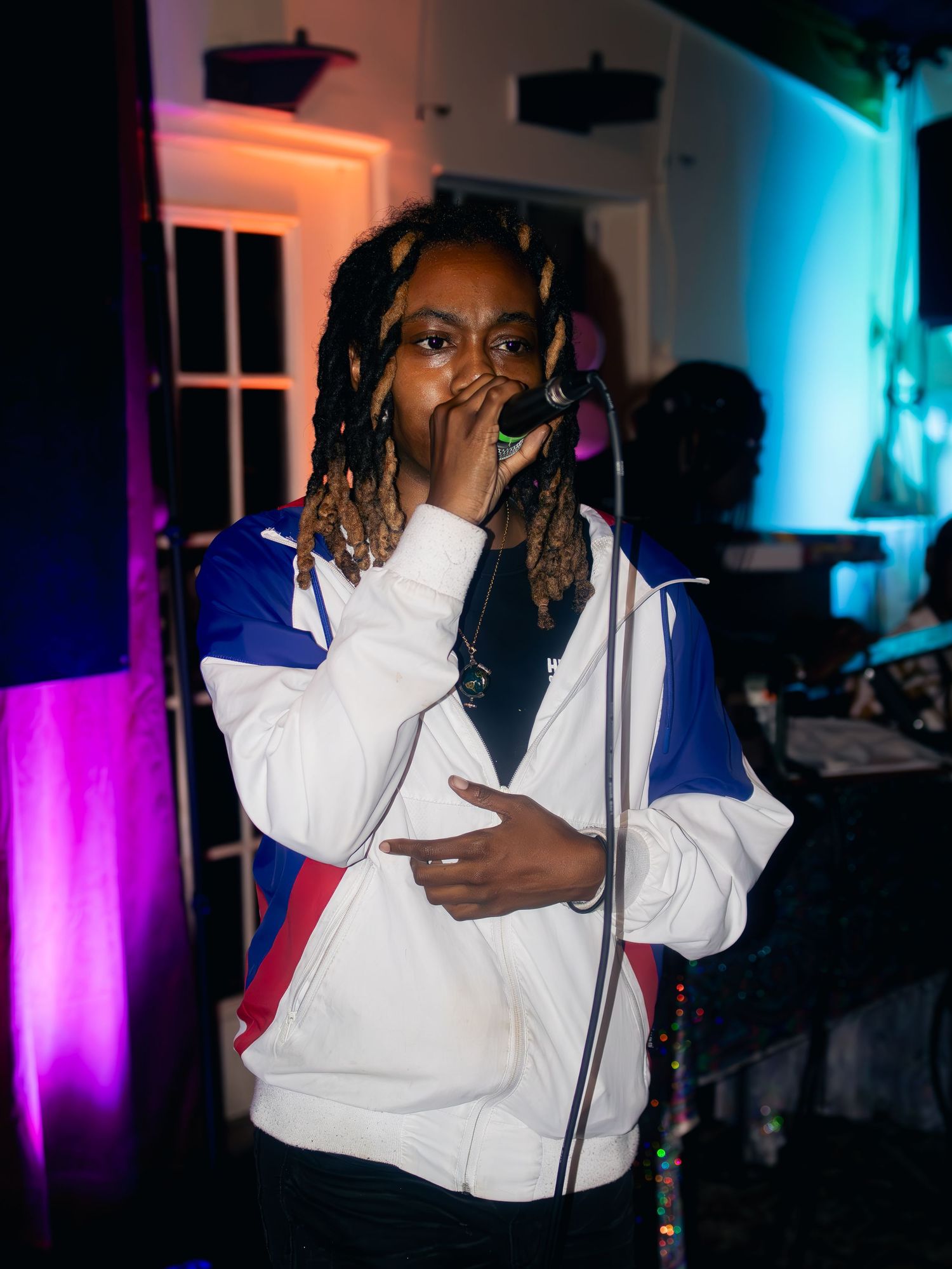 Performer in white and blue jacket singing on stage with purple and blue lighting effects.