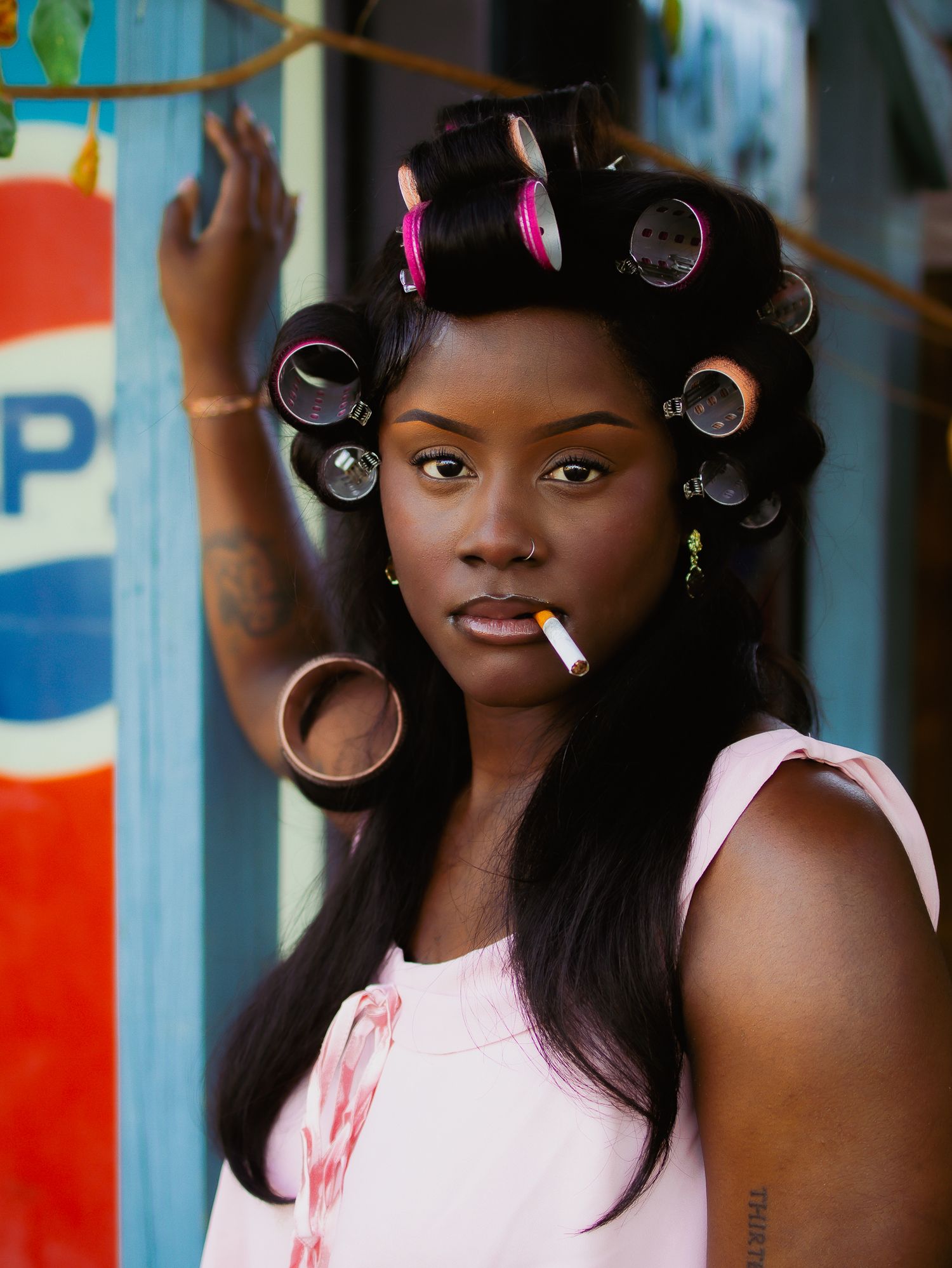 A stylish portrait shows someone wearing rollers and pink against an iconic Pepsi backdrop.