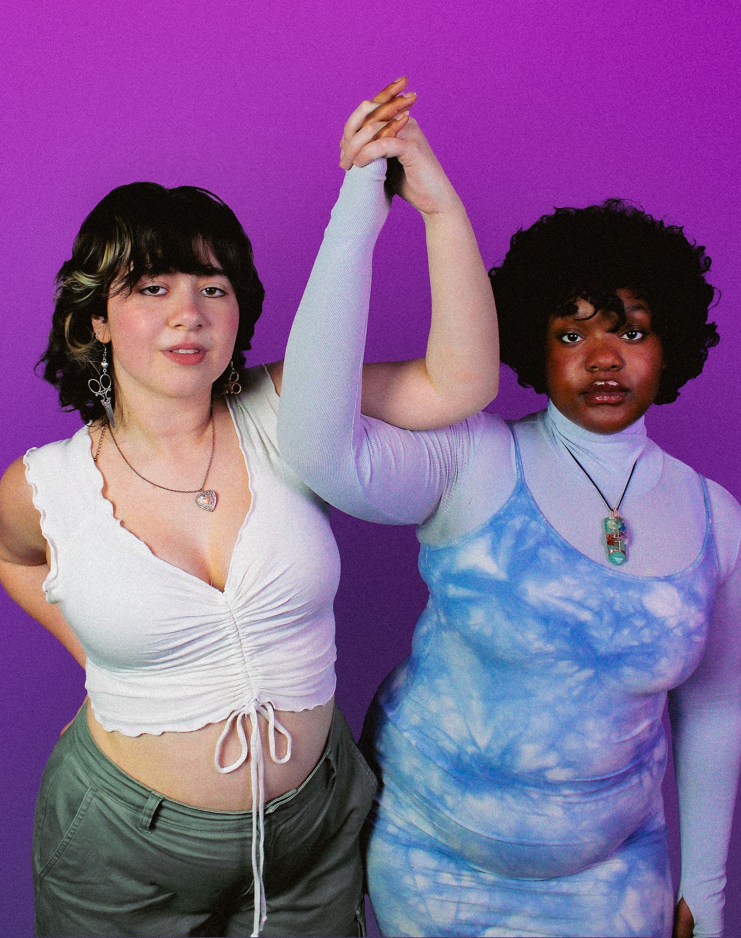 Two young women pose together against a purple background, one in white crop top and one in blue tie-dye outfit.
