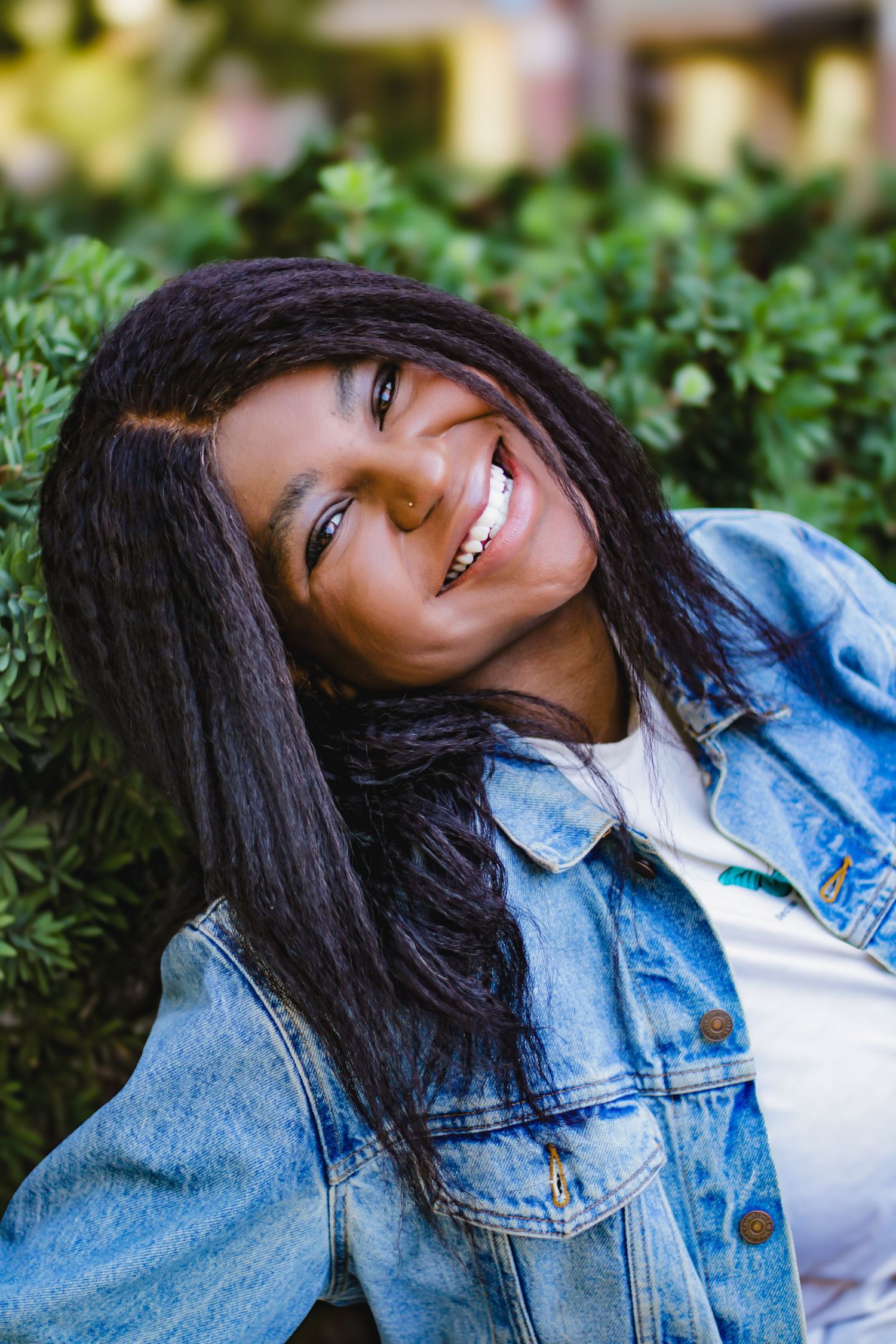 Casual portrait series against greenery wearing denim jacket and white top with natural lighting.