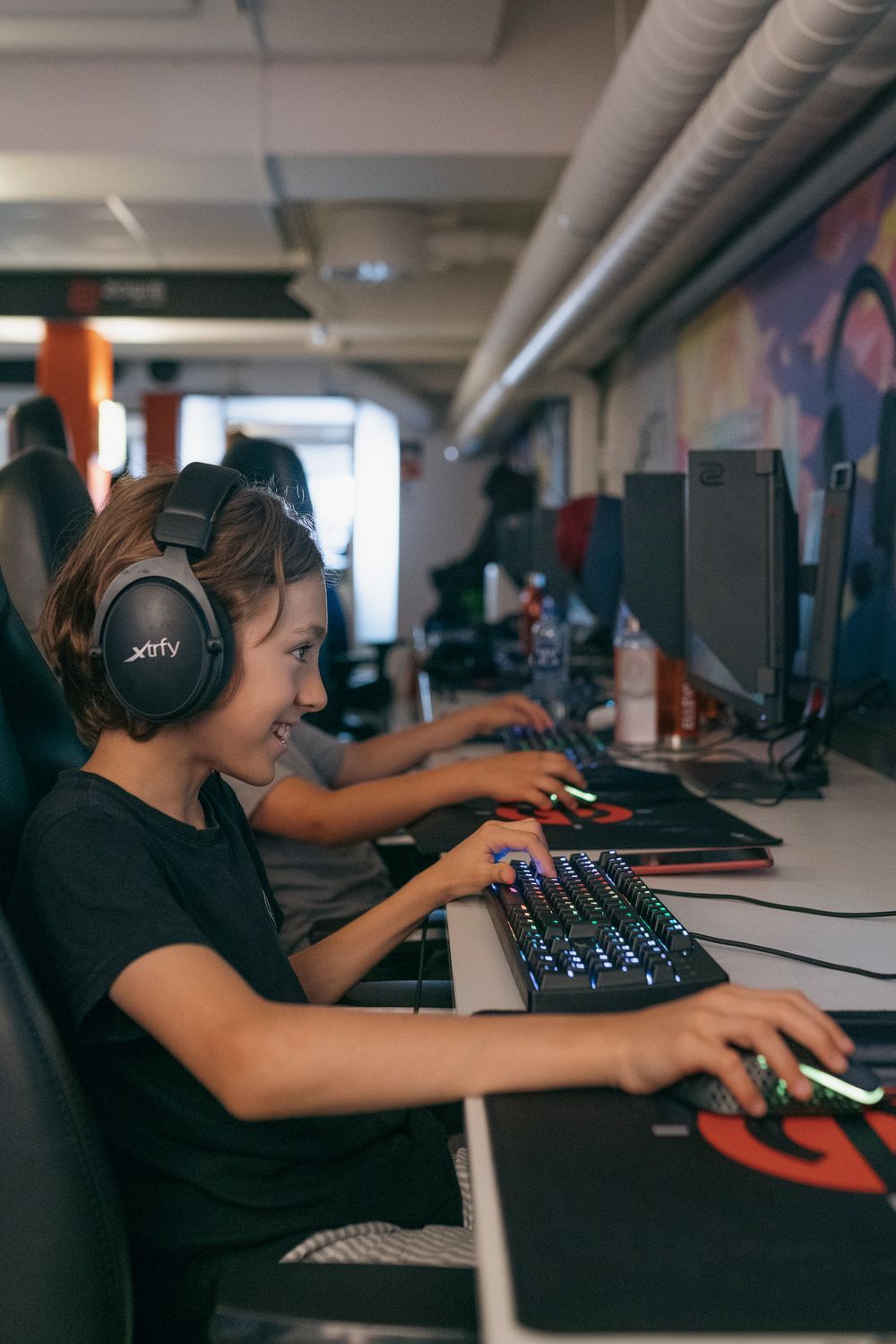 Person wearing headphones sits at computer workstation in office setting with multiple monitors and gaming peripherals.