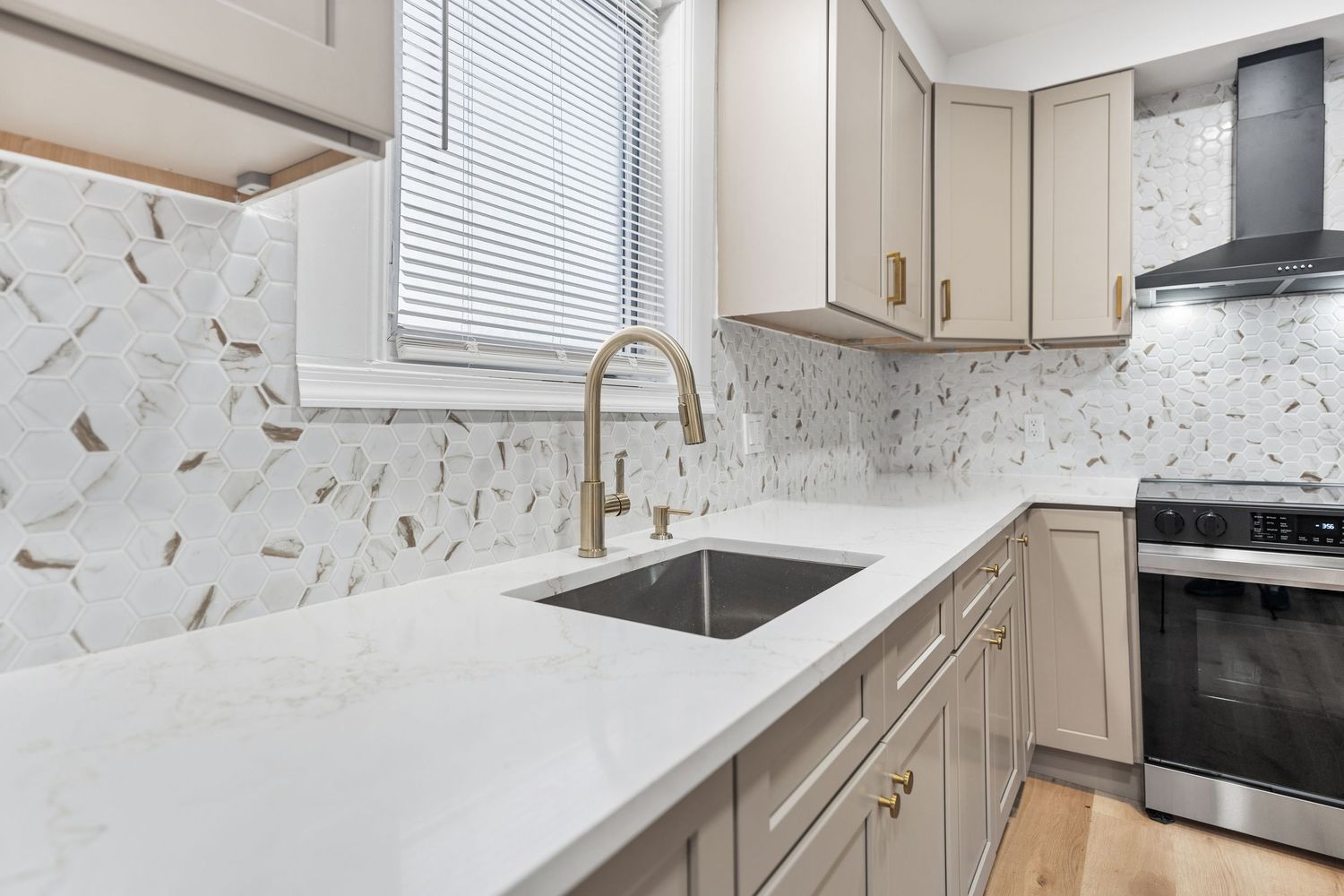 Modern white kitchen with light cabinets, quartz countertops, and geometric tile backsplash featuring a deep undermount sink.