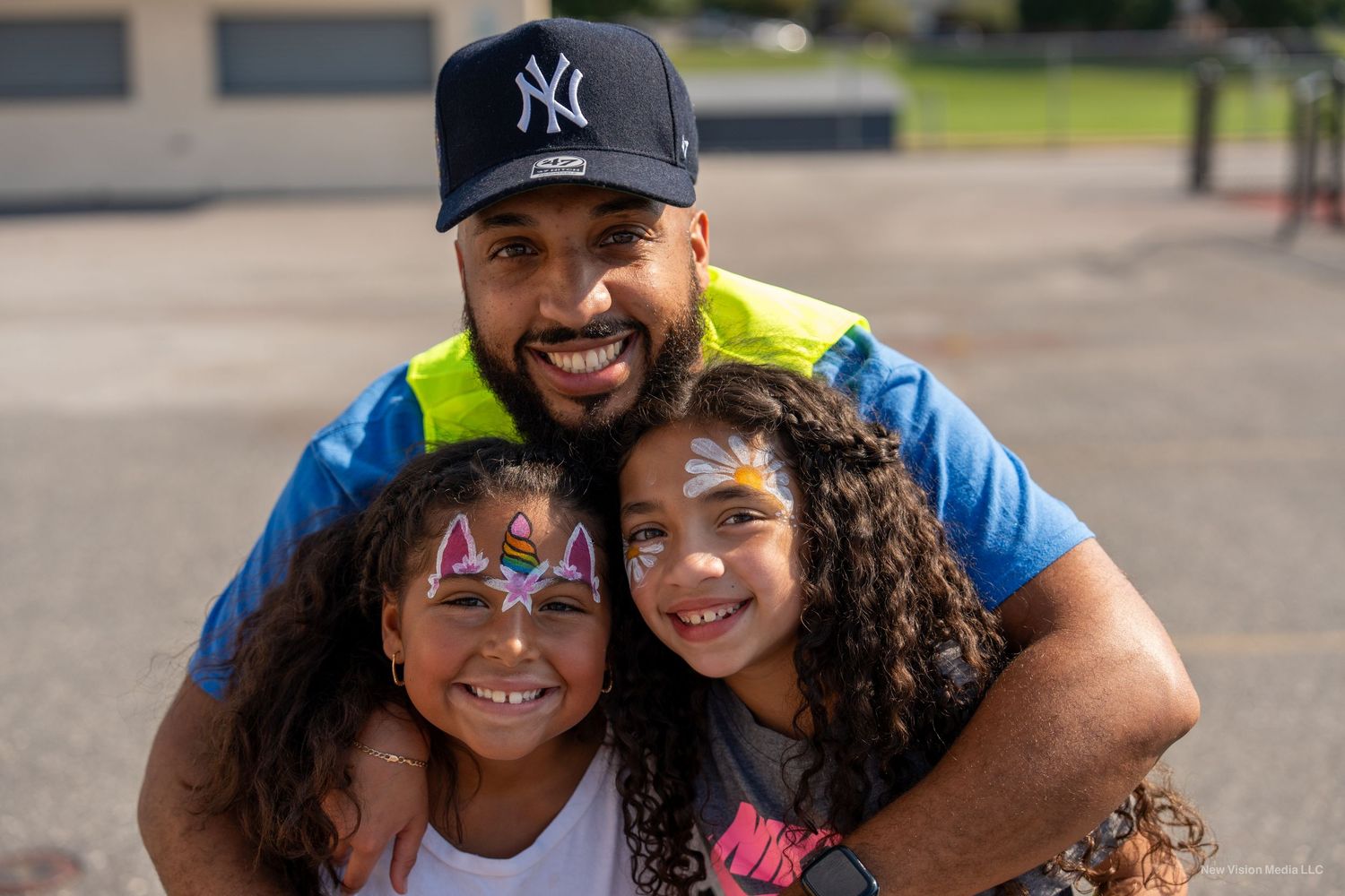 A family smiles together while wearing Yankees baseball caps outdoors.