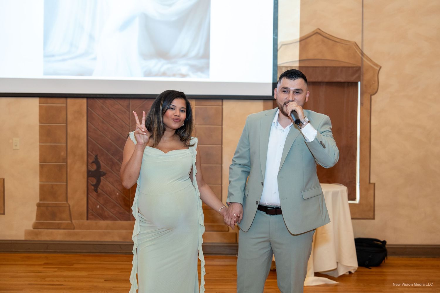 Couple posing at indoor event space with projection screen and wooden details.