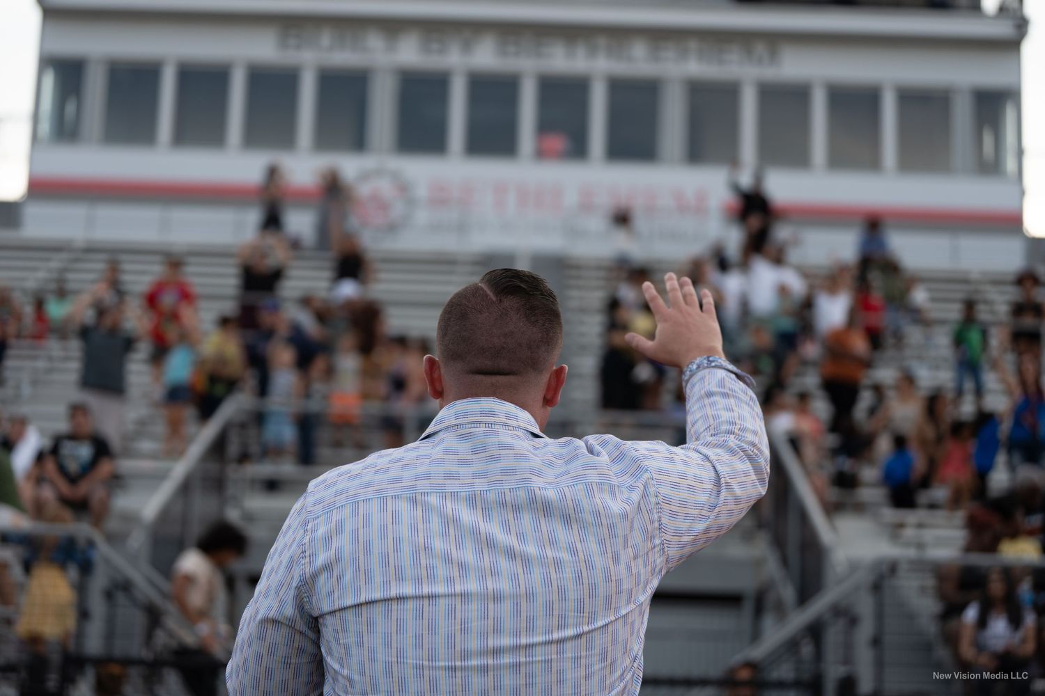 A pastor in a striped shirt gestures while speaking to an audience in stadium bleachers.