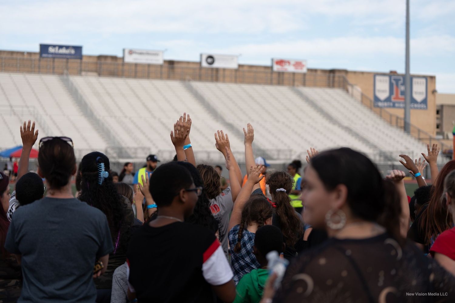 A crowd raises their hands during an outdoor stadium gathering.