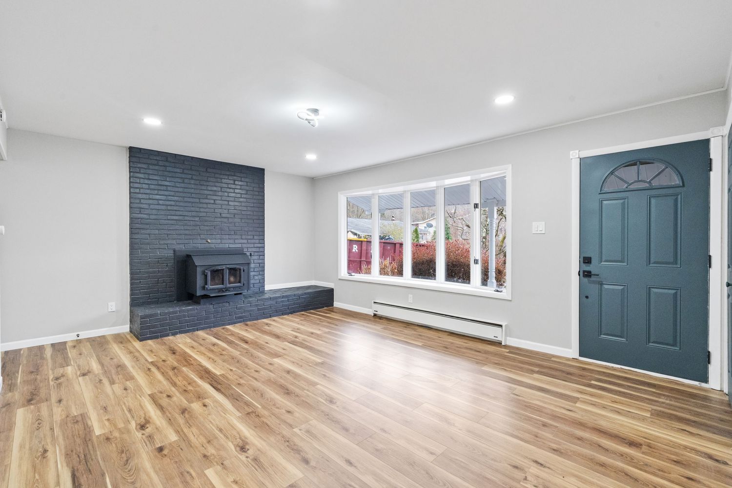 Spacious living room with hardwood floors, black fireplace, and large bay window.