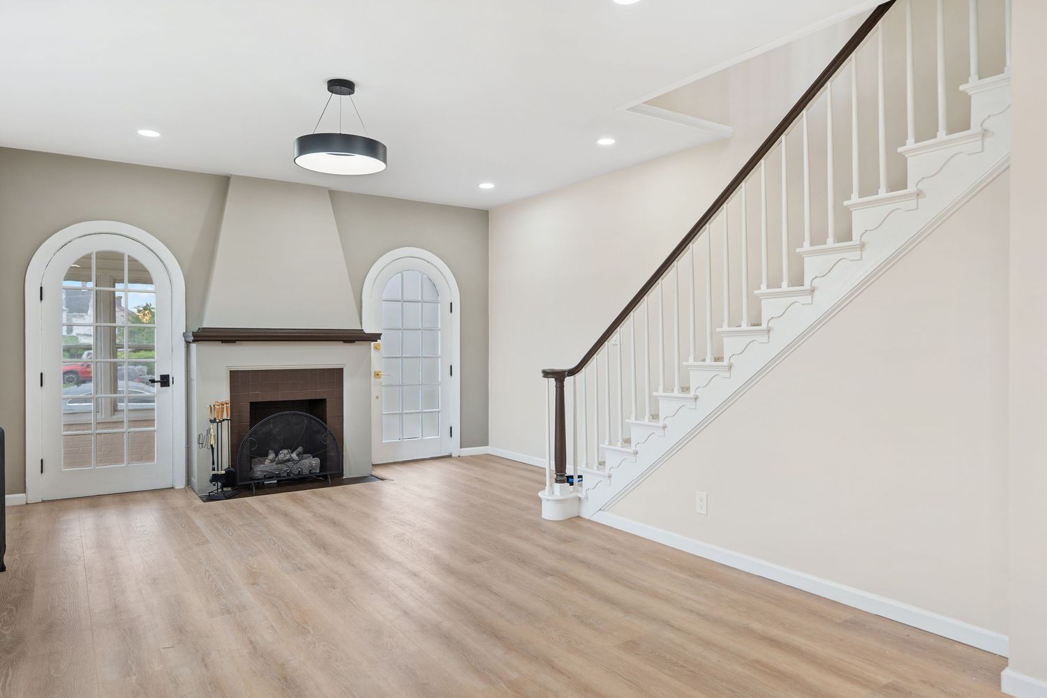 Elegant entryway with white staircase, arched doorway, and built-in fireplace on hardwood floors.