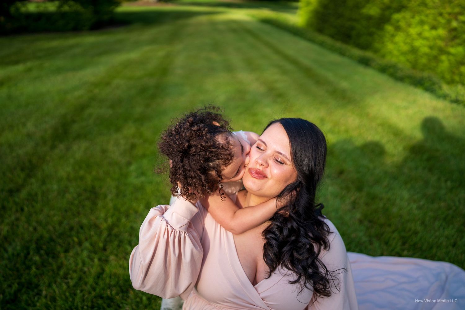 Joyful candid moment between mother and child laying on grass in garden setting.