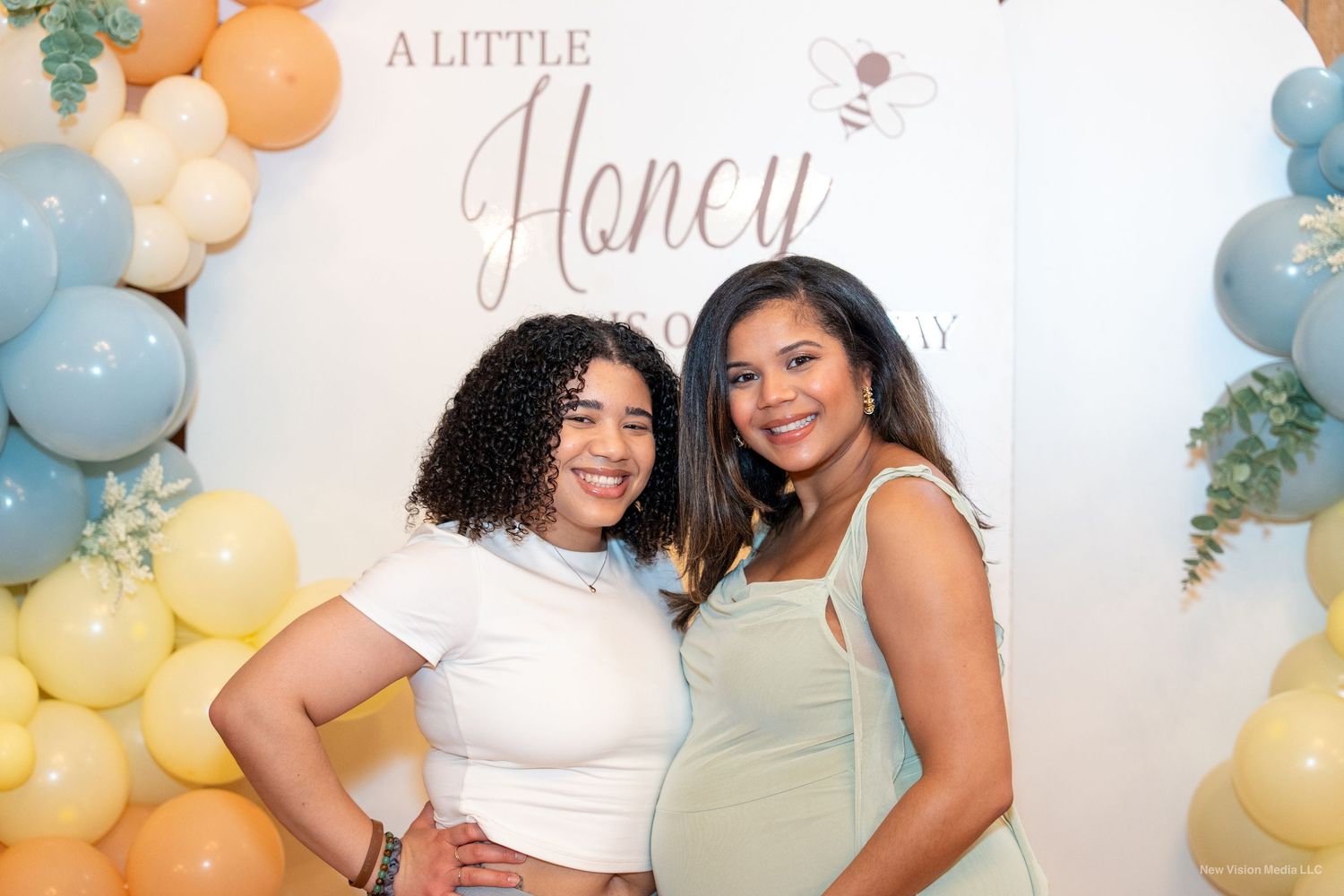 Baby shower setting with pastel balloon arch and text reading 'A Little Honey'.