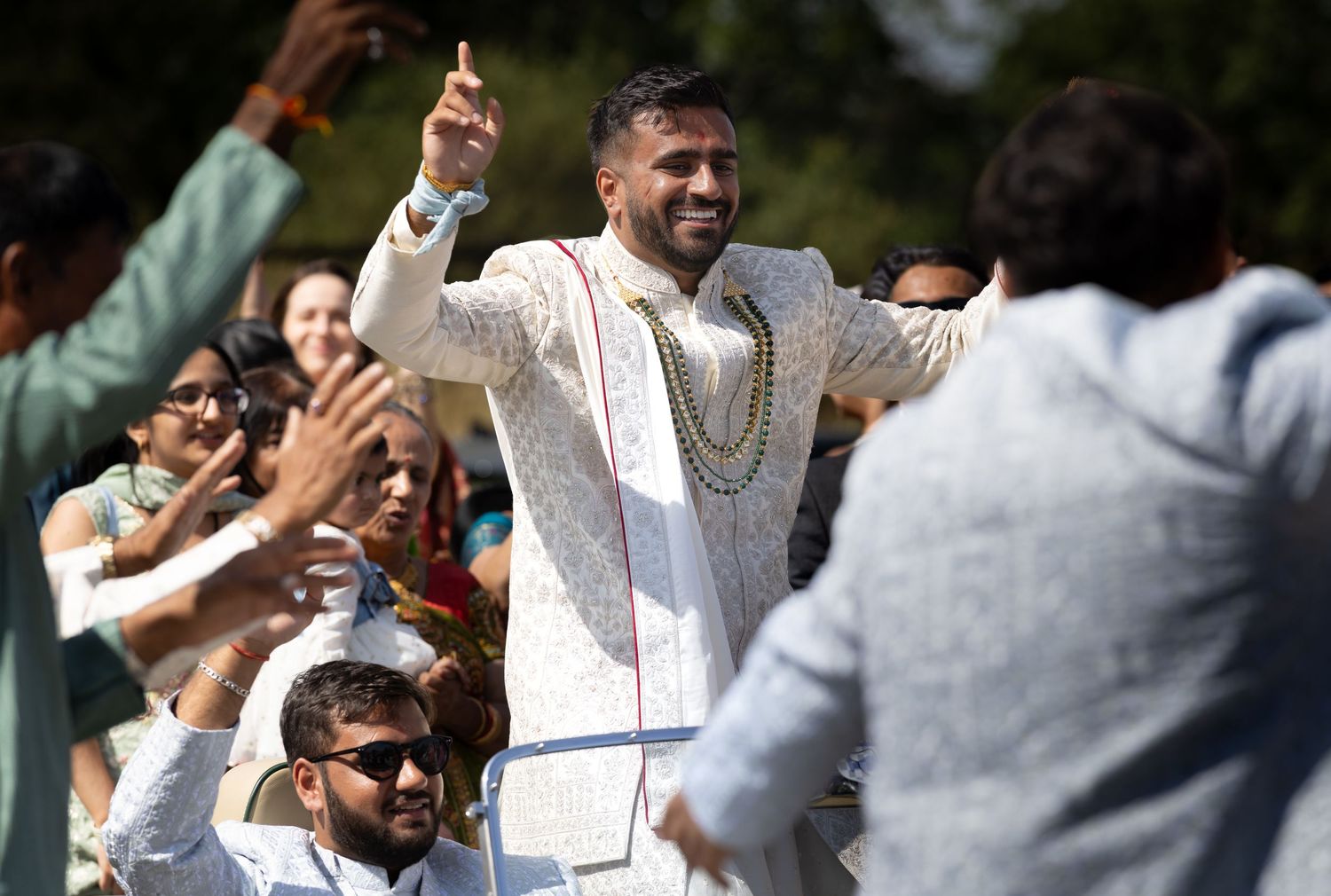 Groom in traditional Indian sherwani celebrates joyfully with guests during wedding baraat procession.