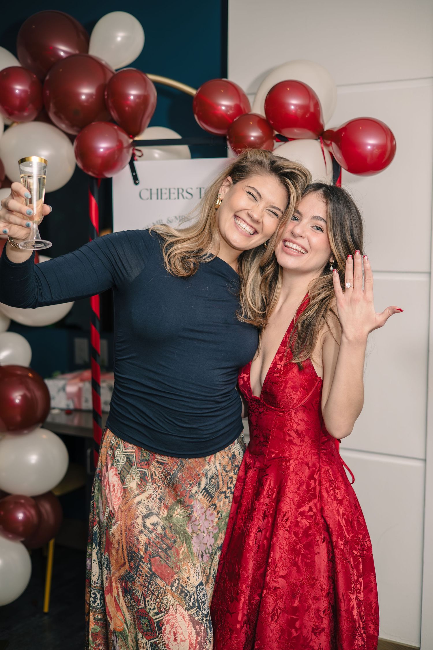 Two friends celebrate with red and white balloons at a festive party in formal attire.