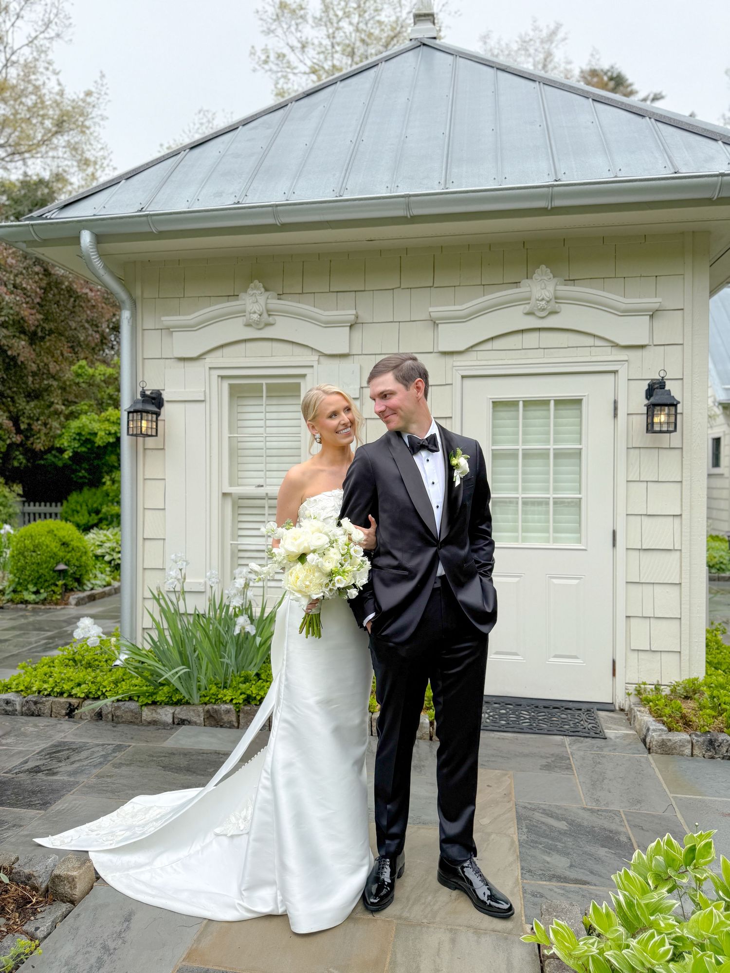 An elegant couple poses outside a white garden pavilion with classic architectural details.