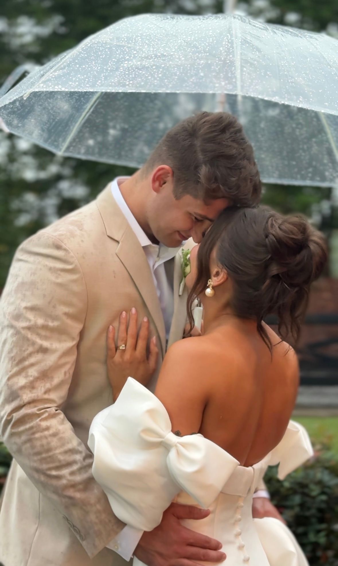 A romantic moment under a clear umbrella during a rainy wedding day.