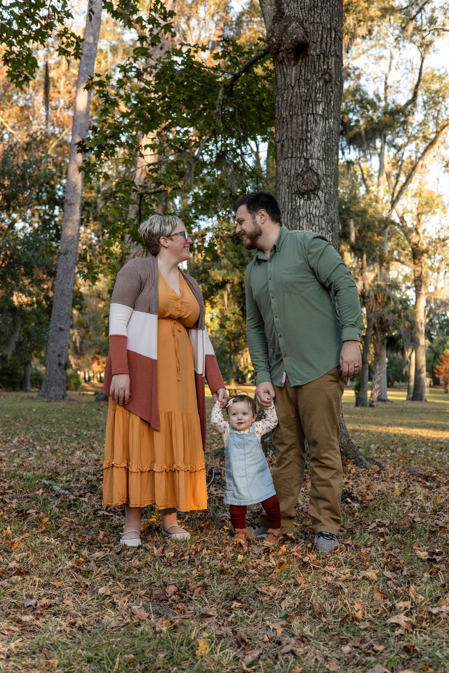 Family in autumn outfits poses together in park with fallen leaves.