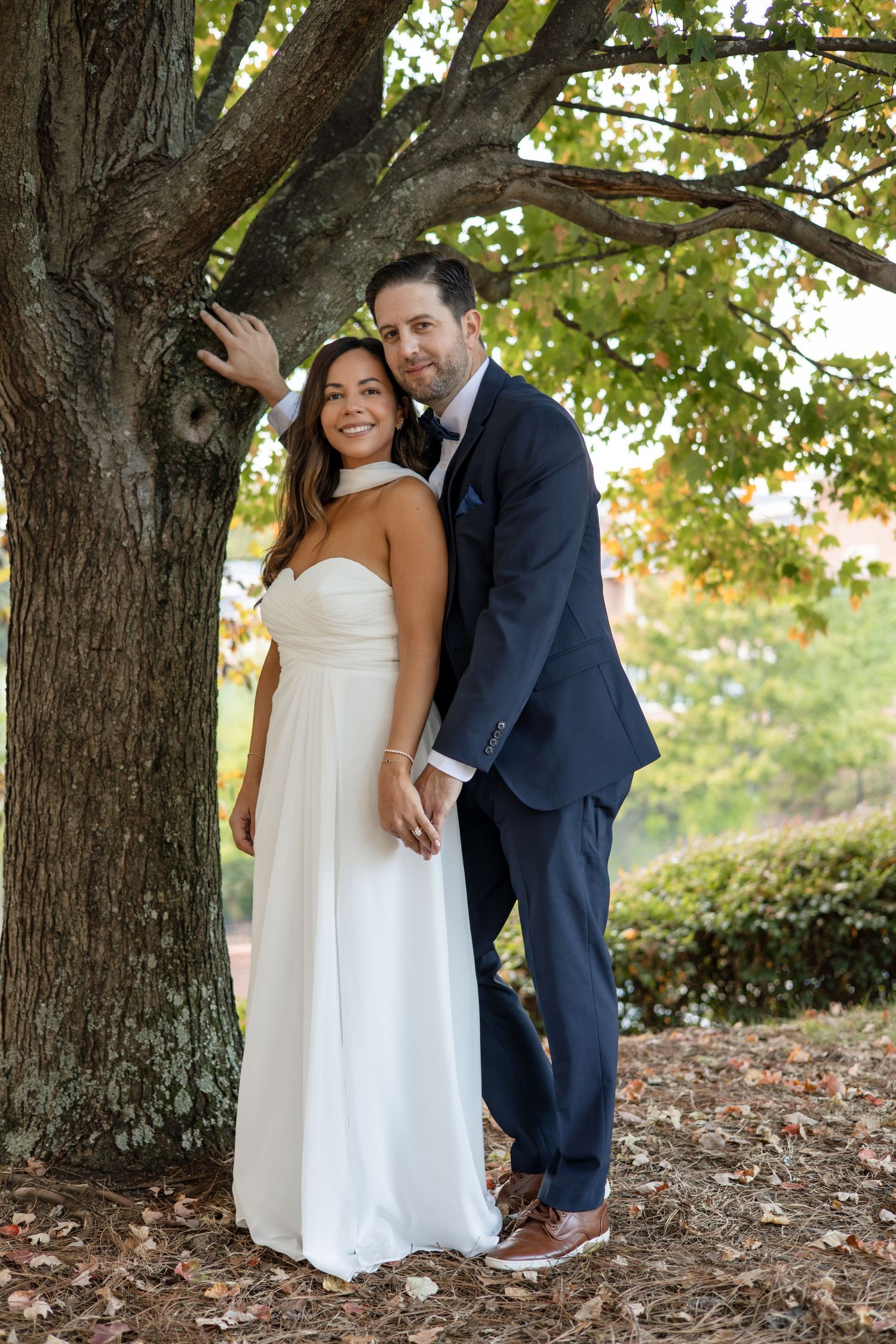 A couple sharing intimate moments under large trees with fallen leaves.
