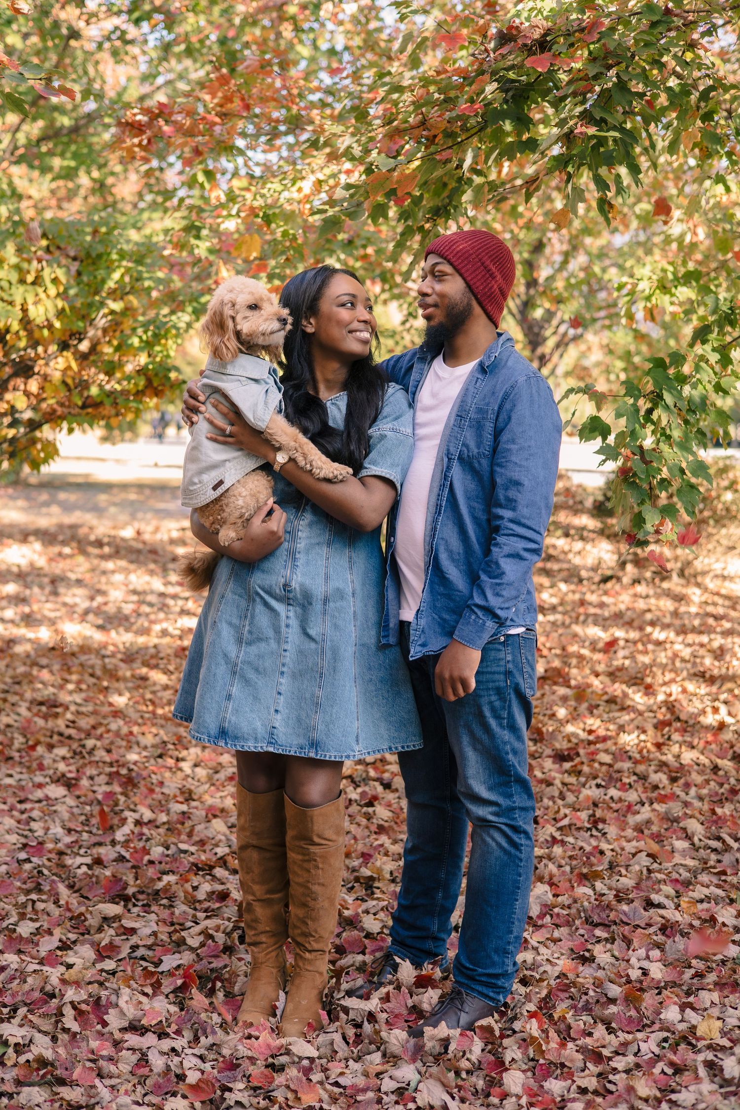 Couple holding their dog while enjoying autumn scenery outdoors.