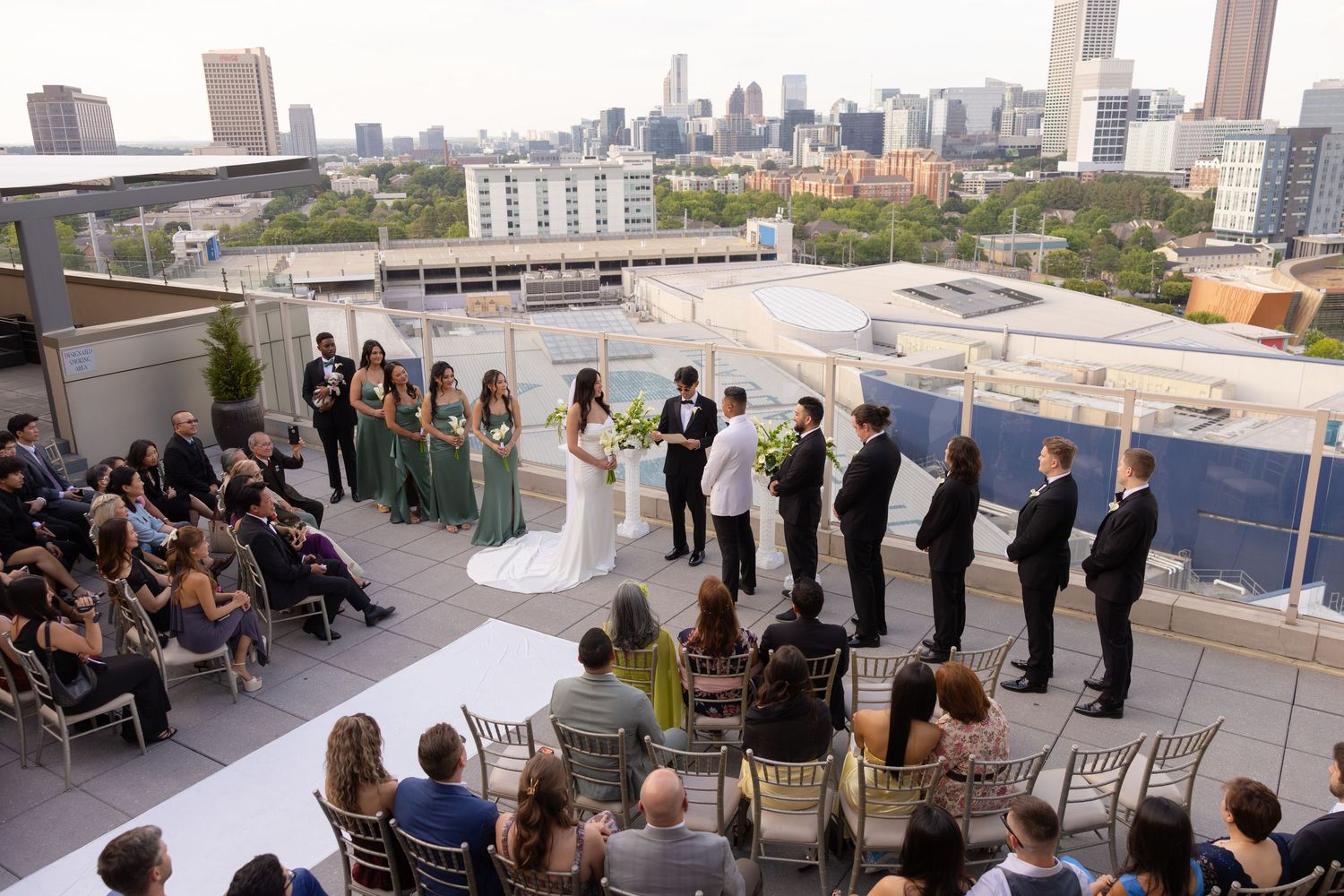 Rooftop wedding ceremony with bridal party and guests against Atlanta city skyline backdrop.