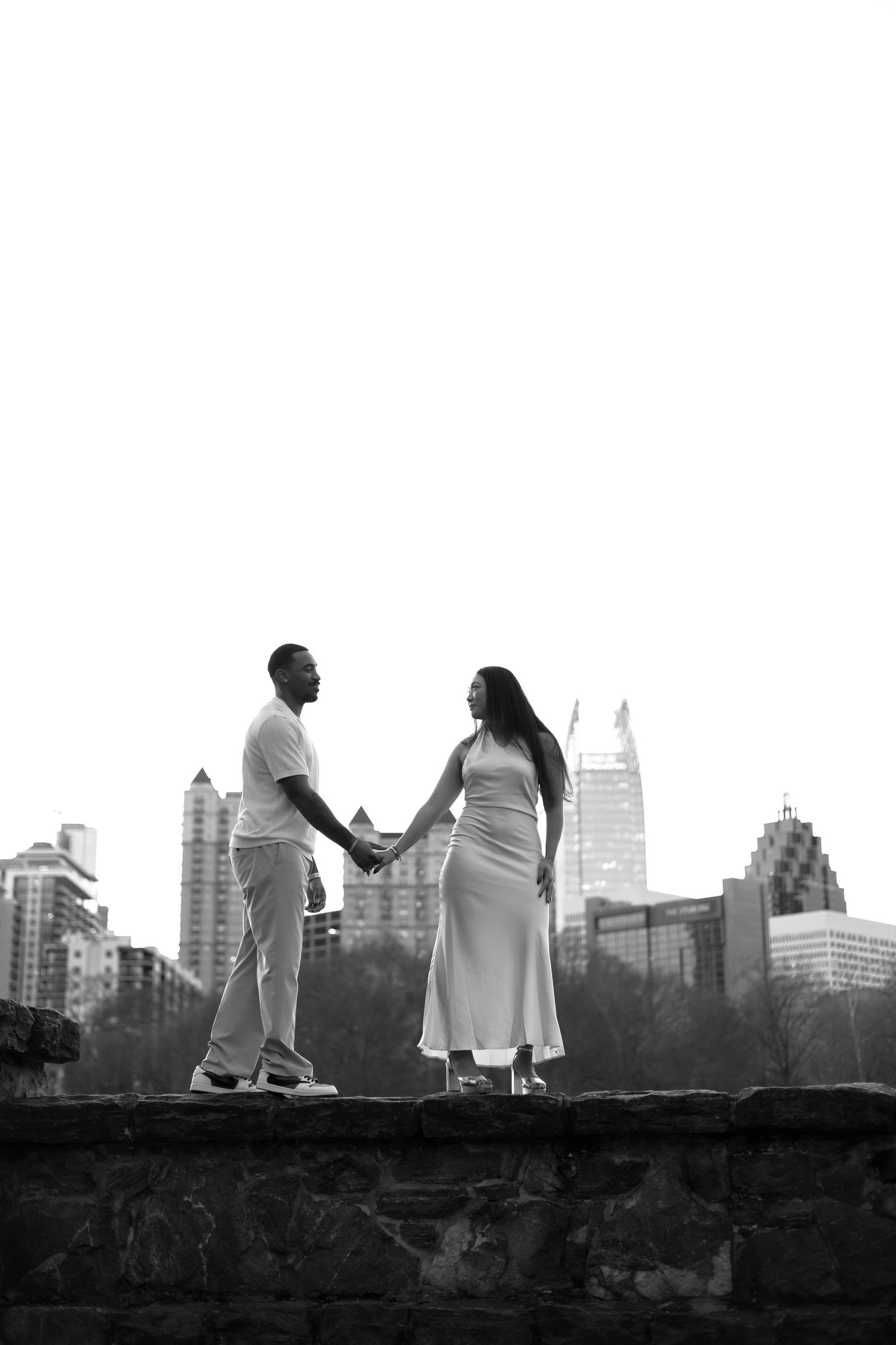 Silhouettes of people standing on a stone wall against a city skyline at dusk in black and white.